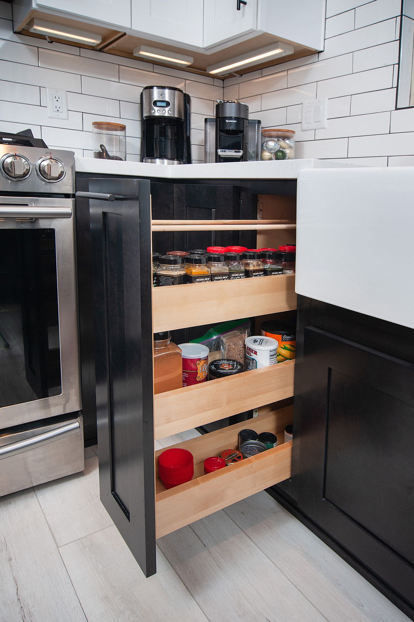 Black cabinet with pull-out shelves, holding spices and kitchen items next to a stove and sink.
