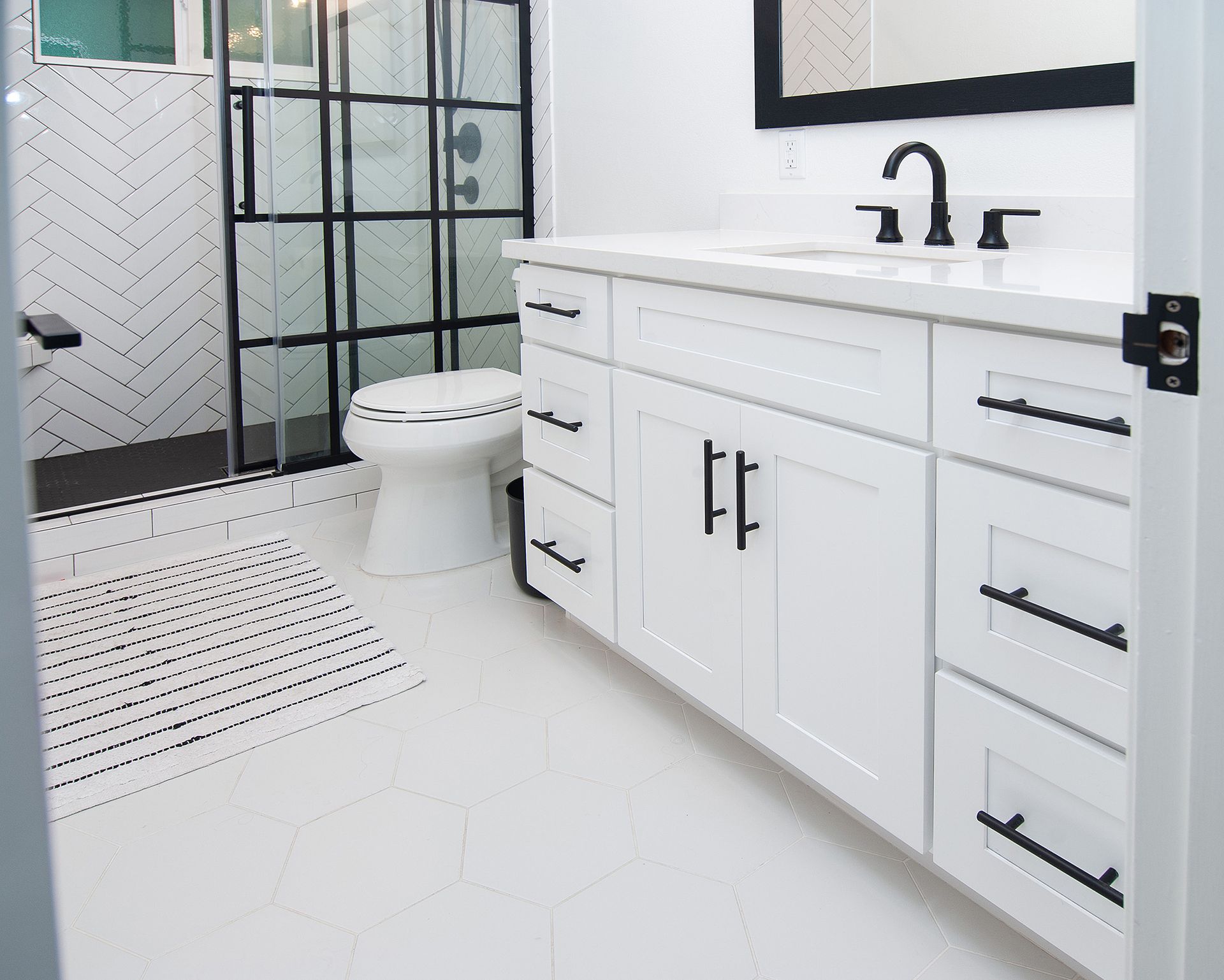 White bathroom with black accents. Includes a glass shower, white vanity, toilet, and black hardware.