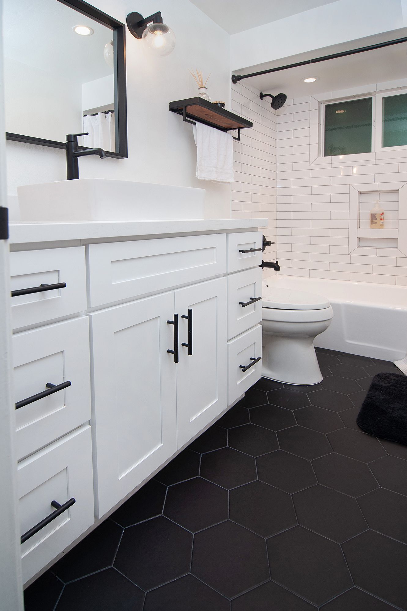 Modern bathroom with white vanity, black hexagon floor tiles, and textured white wall.