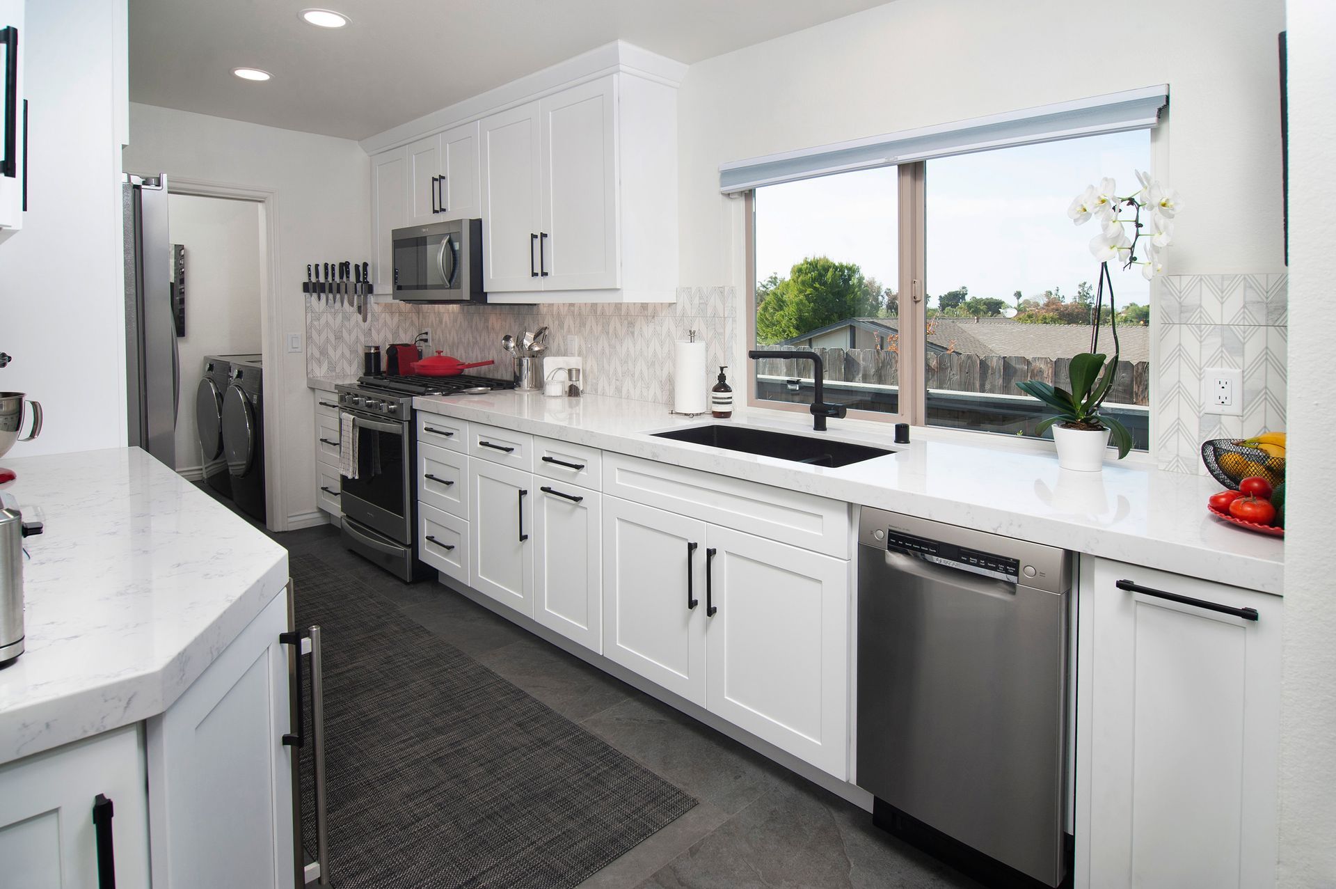 White kitchen with stainless steel appliances, black hardware, and a large window.