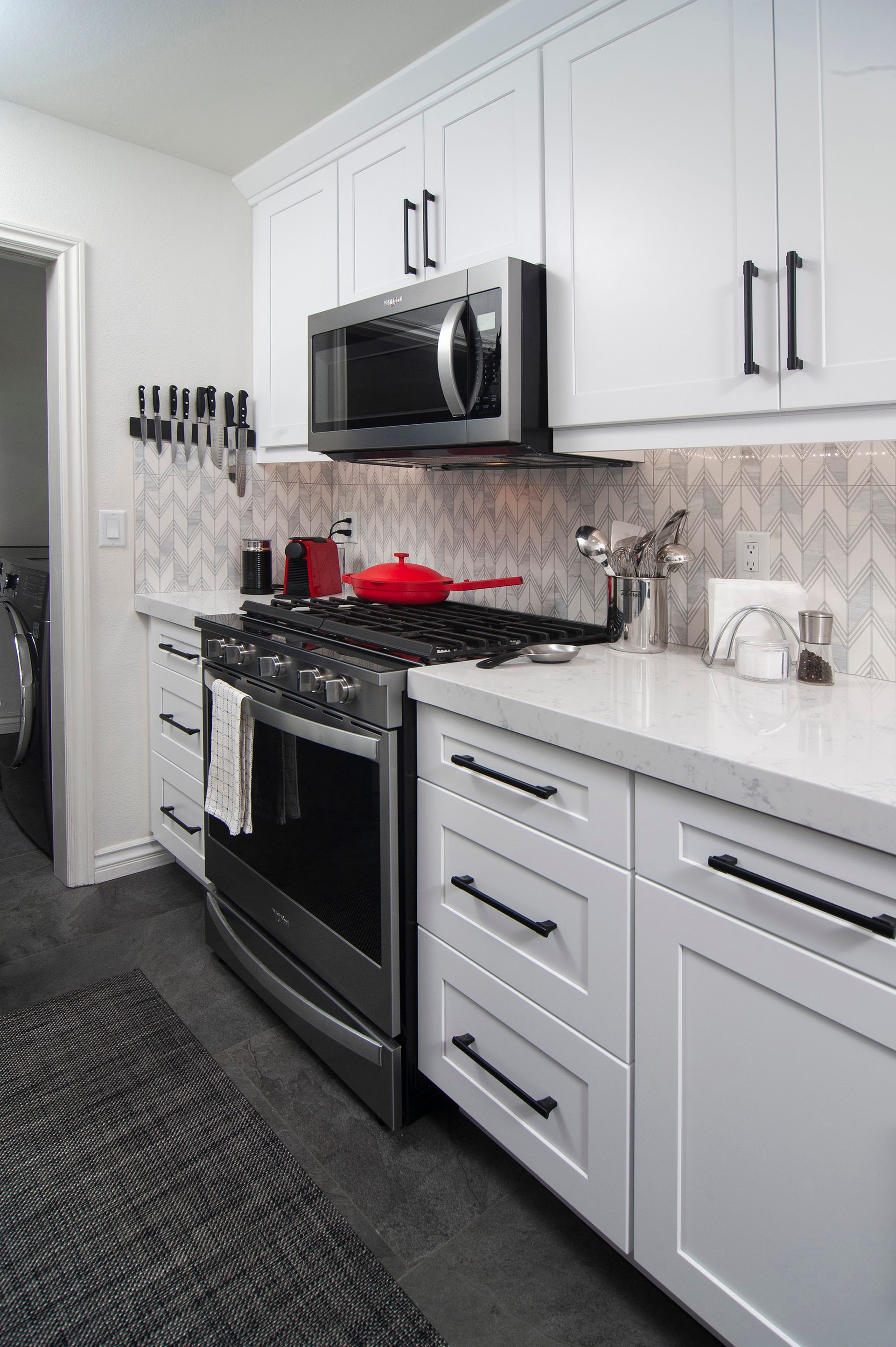 White kitchen with stainless steel appliances, black hardware, and light-colored countertops.