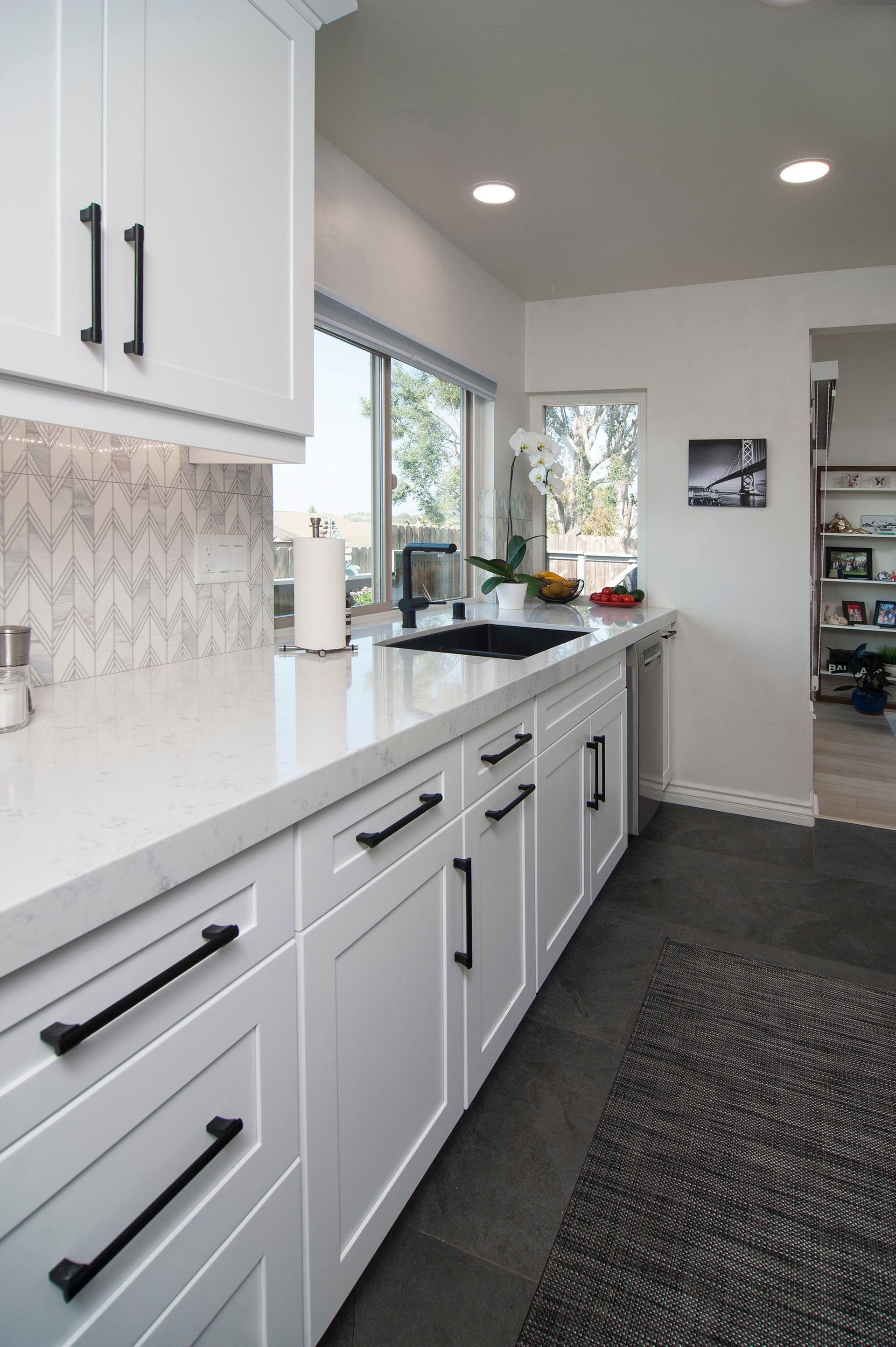 White kitchen with black hardware, countertops, and sink. Gray tile floor.