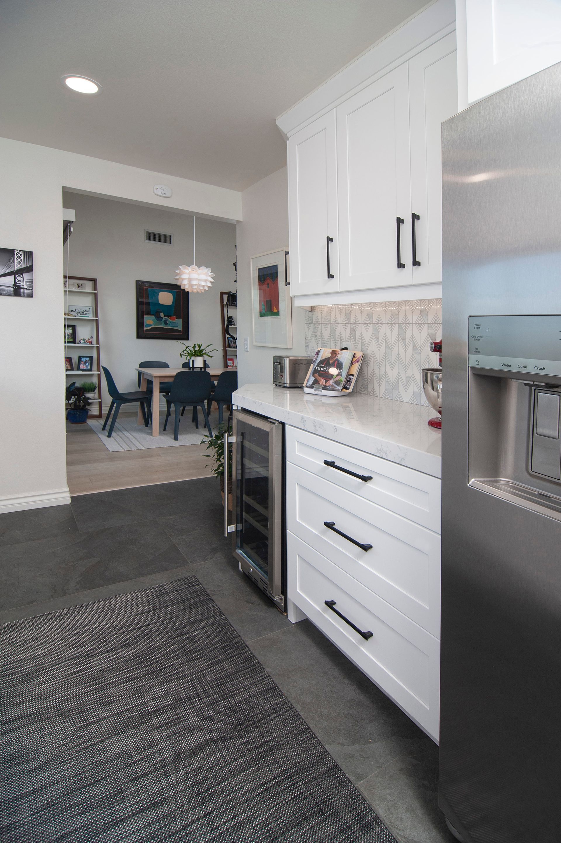 Modern kitchen with white cabinets, stainless steel appliances, and a view into a dining room.