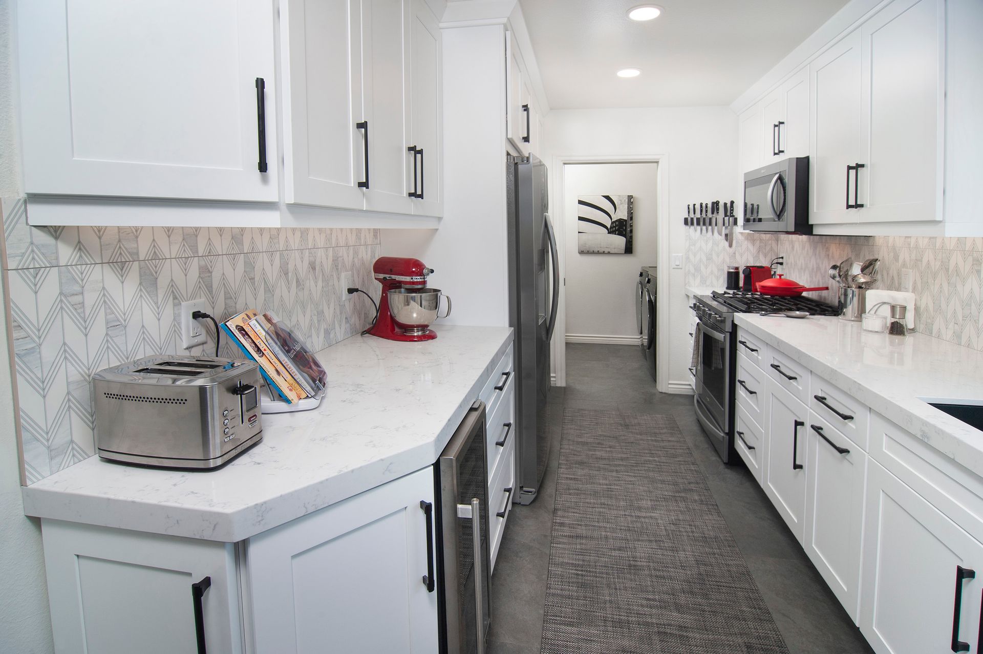 White kitchen with stainless steel appliances, two counters, and a long hallway.