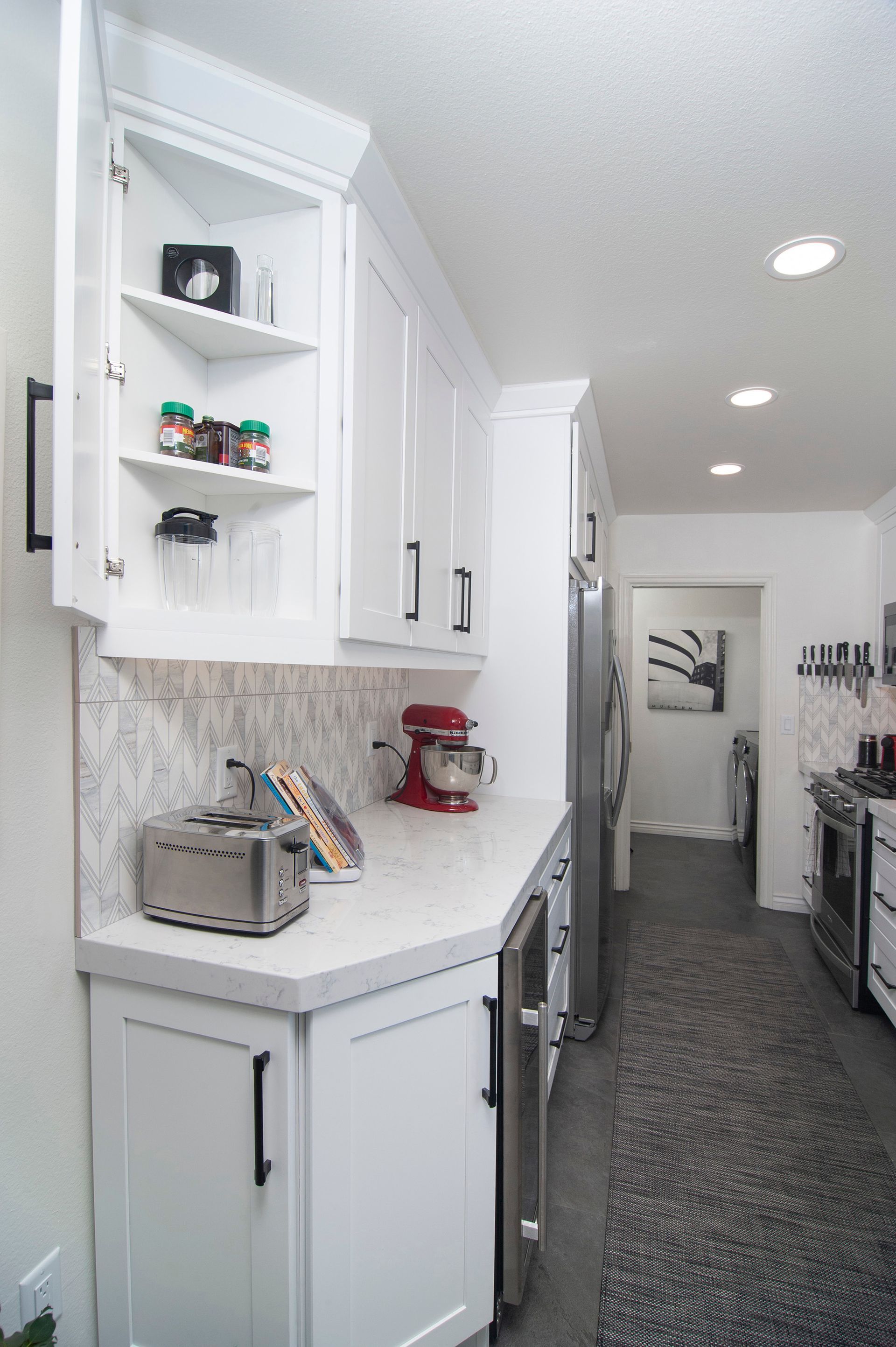 White kitchen with corner cabinets, countertop, and appliances along a narrow hallway.