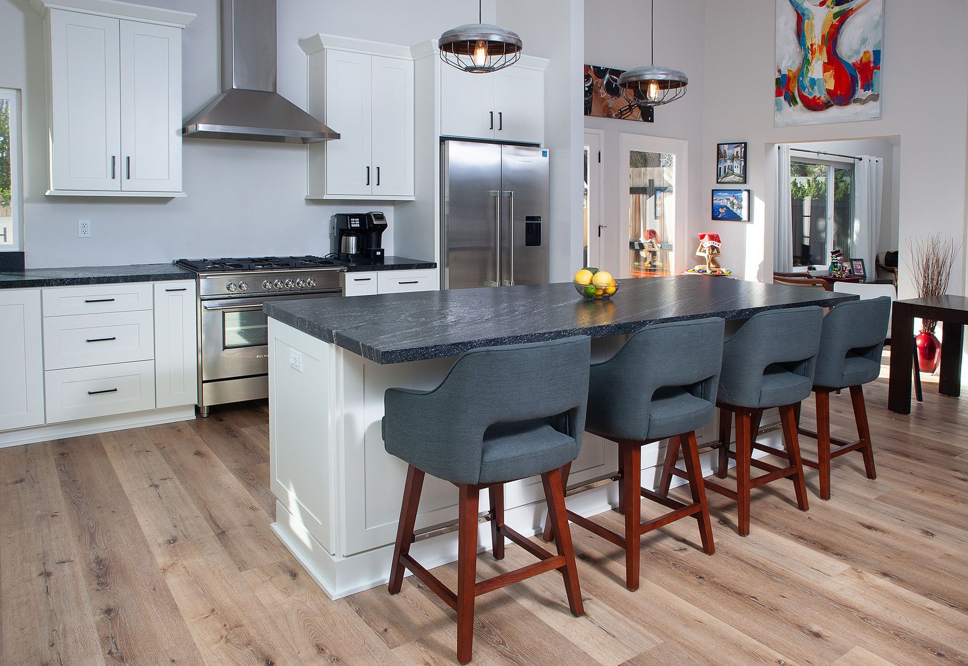 Modern kitchen with white cabinets, island with seating, stainless steel appliances, and wood flooring.