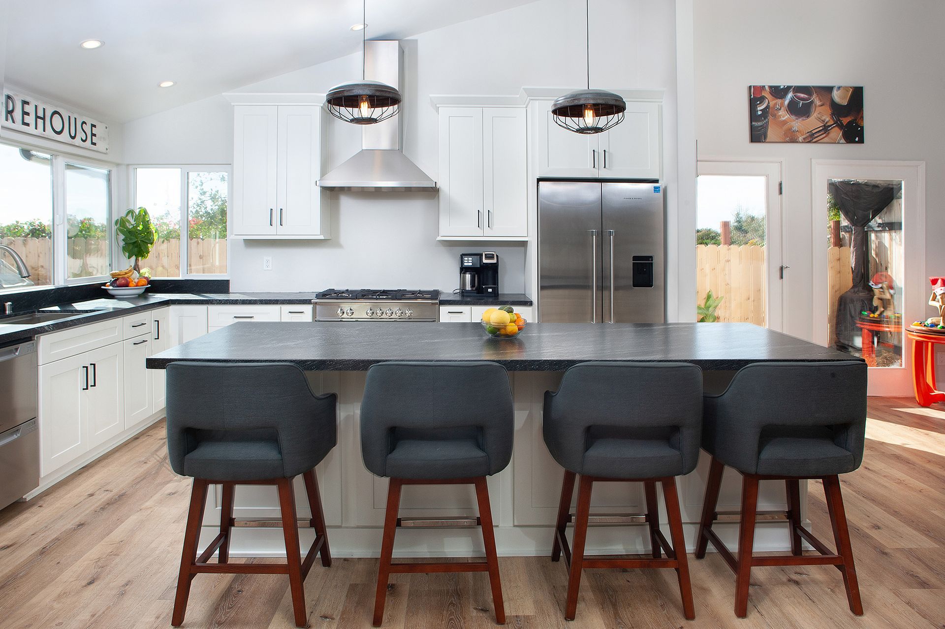 Modern kitchen with gray island, white cabinets, stainless appliances, and four gray stools.