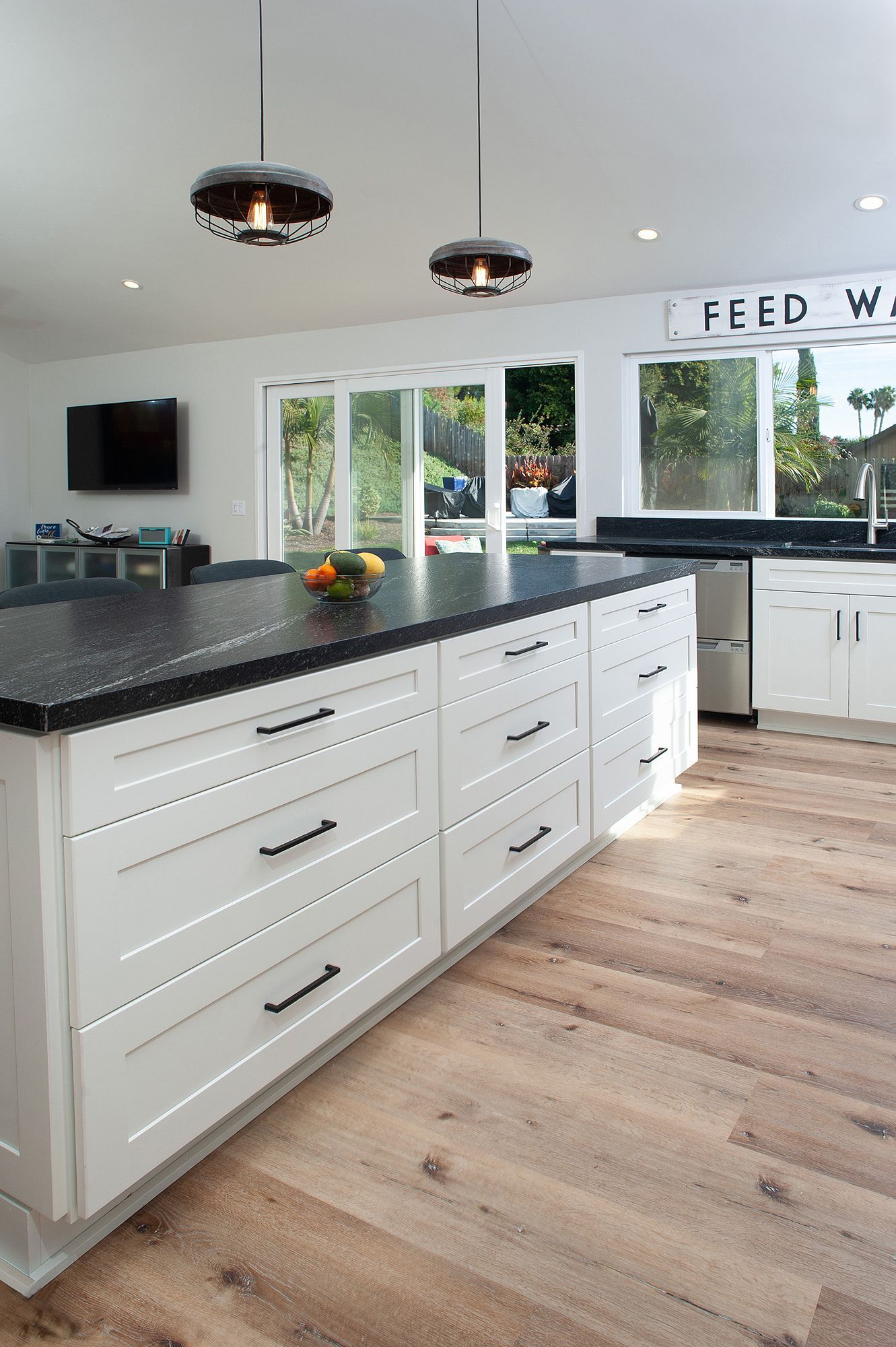 White kitchen with a black countertop island, hardwood floors, and modern light fixtures.