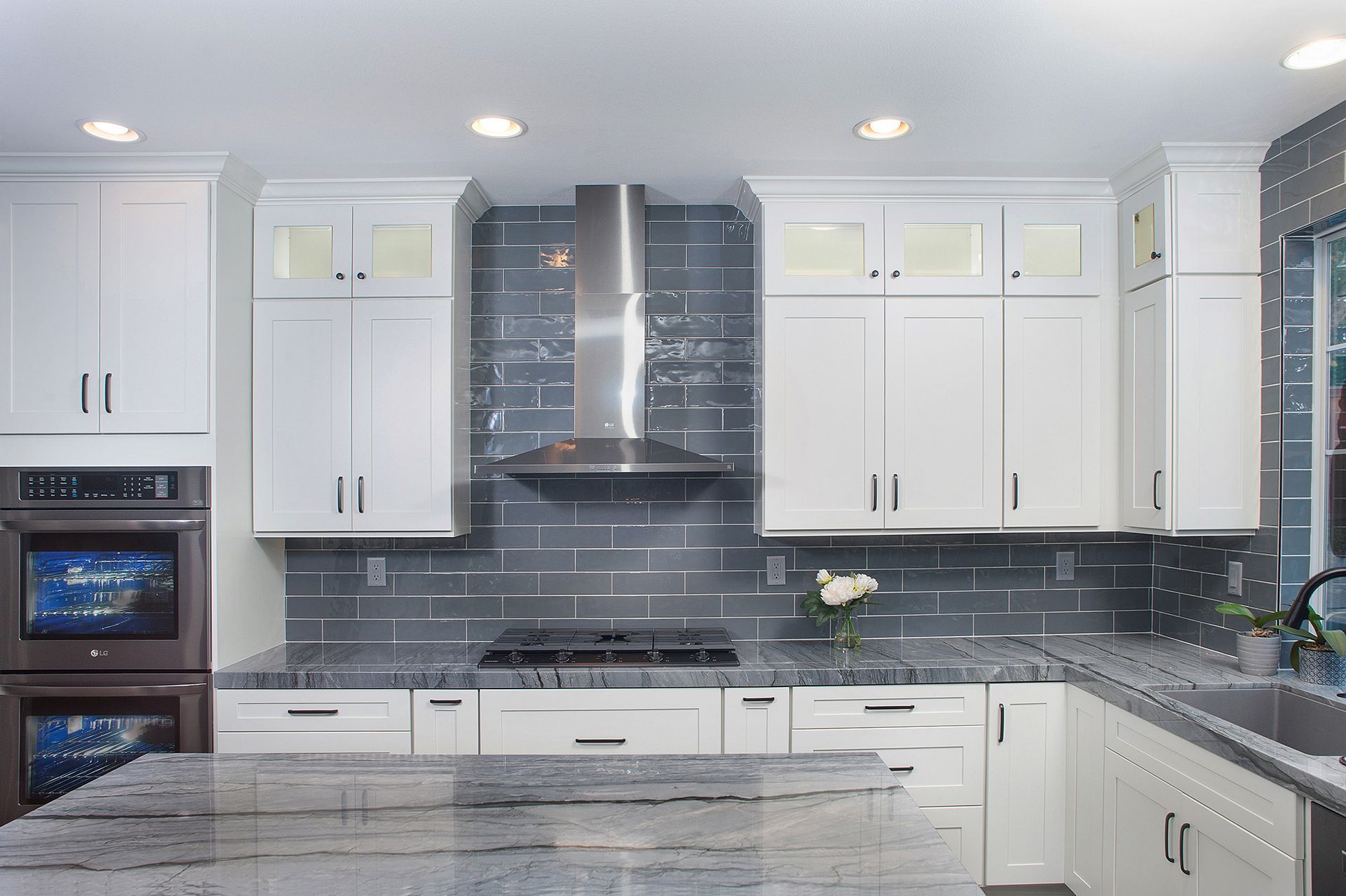 White kitchen with gray backsplash, stainless steel range hood, and granite countertops.