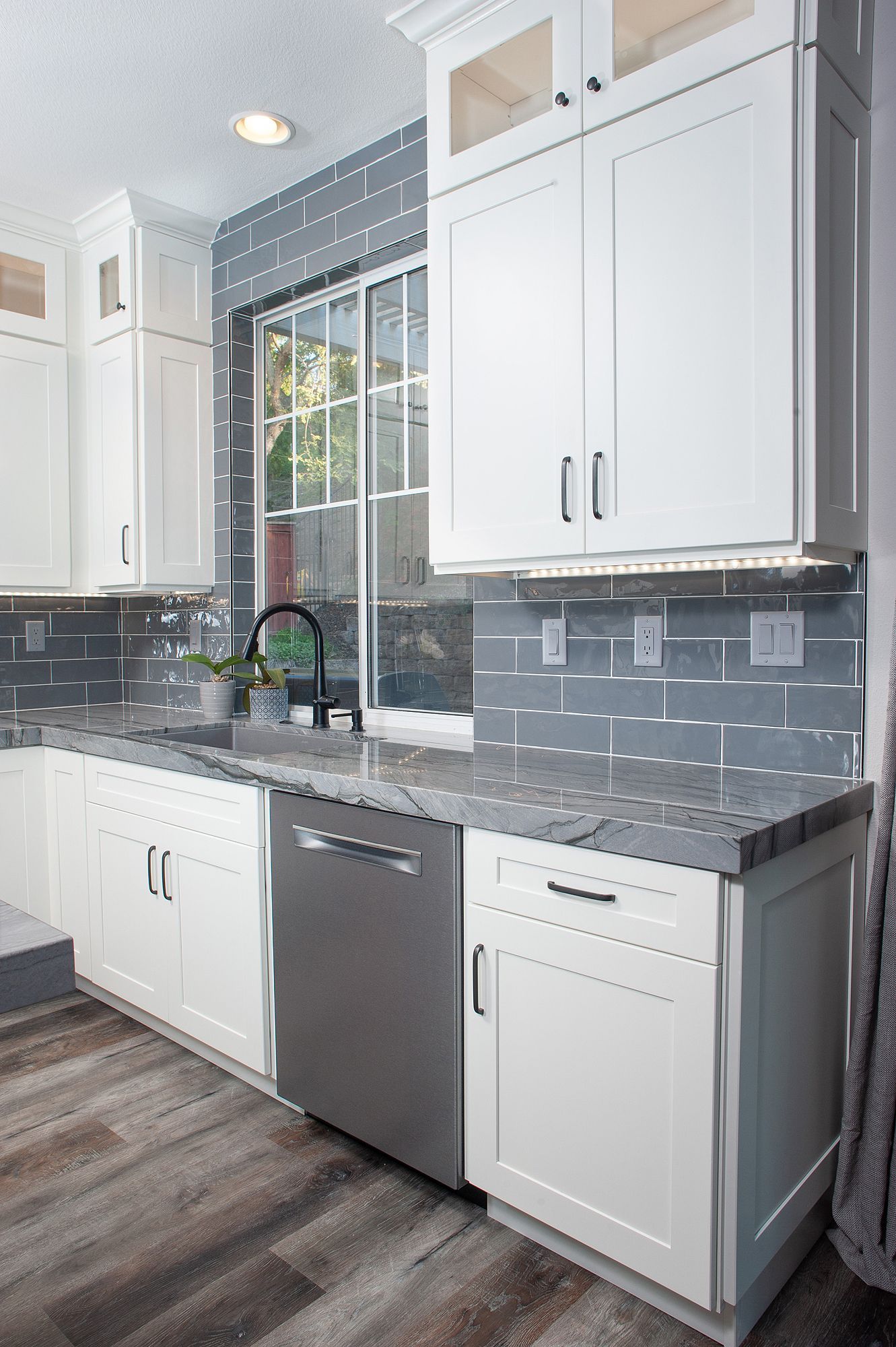 White kitchen with gray backsplash, stainless steel dishwasher, and wooden floor.
