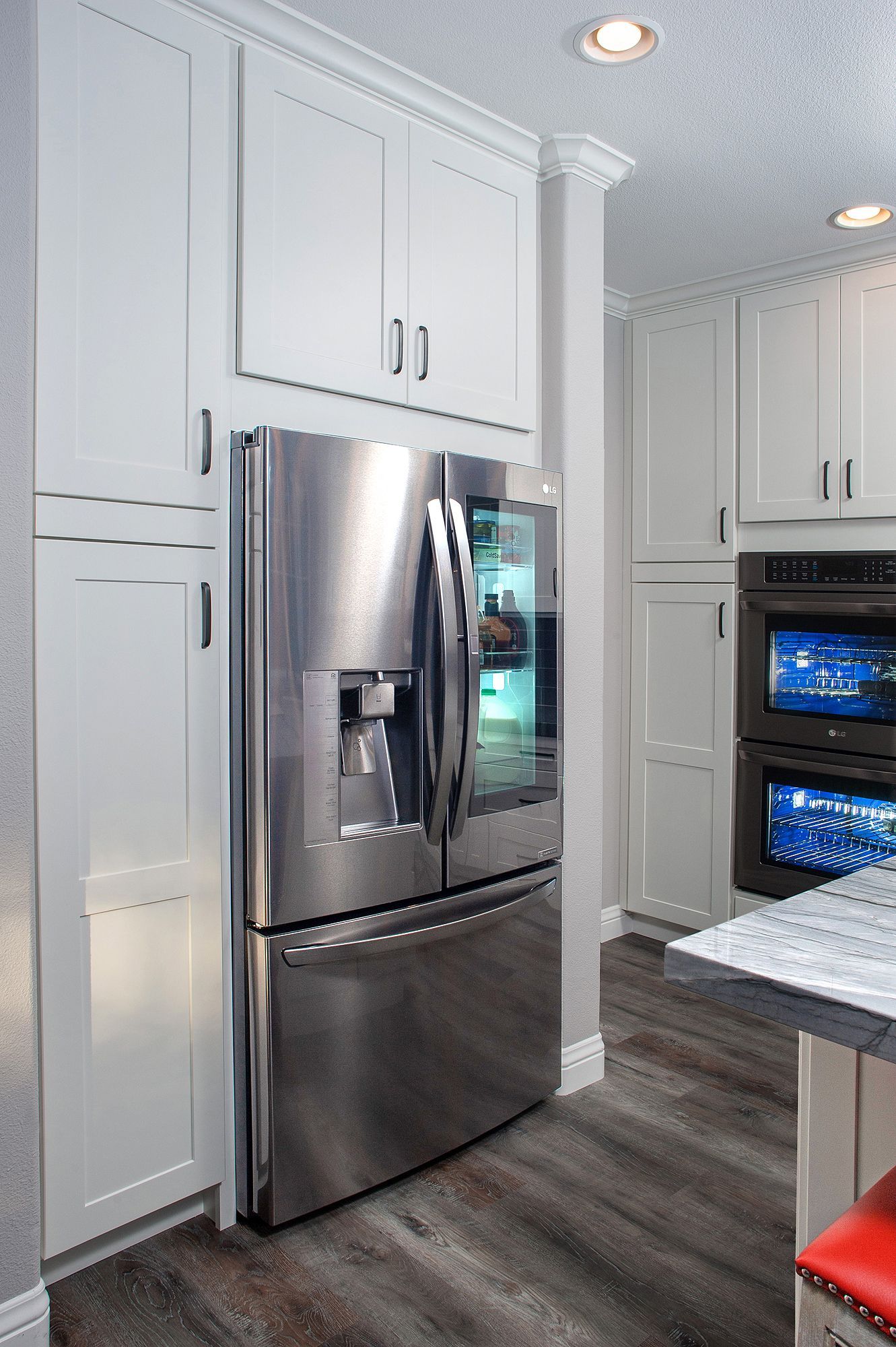 Stainless steel refrigerator flanked by white kitchen cabinets in a modern kitchen.