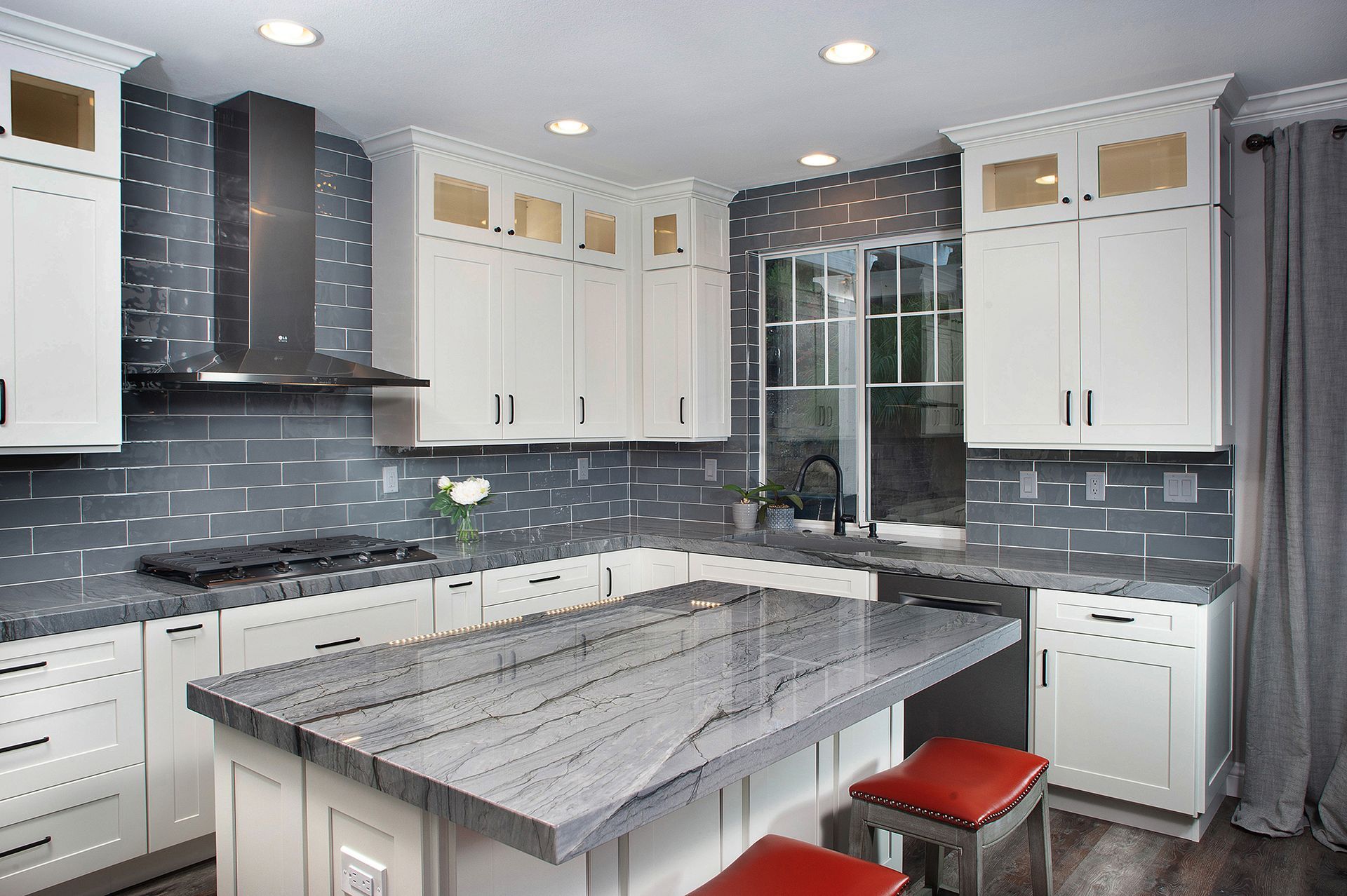 White kitchen with gray backsplash, island, and granite countertop; two red stools.