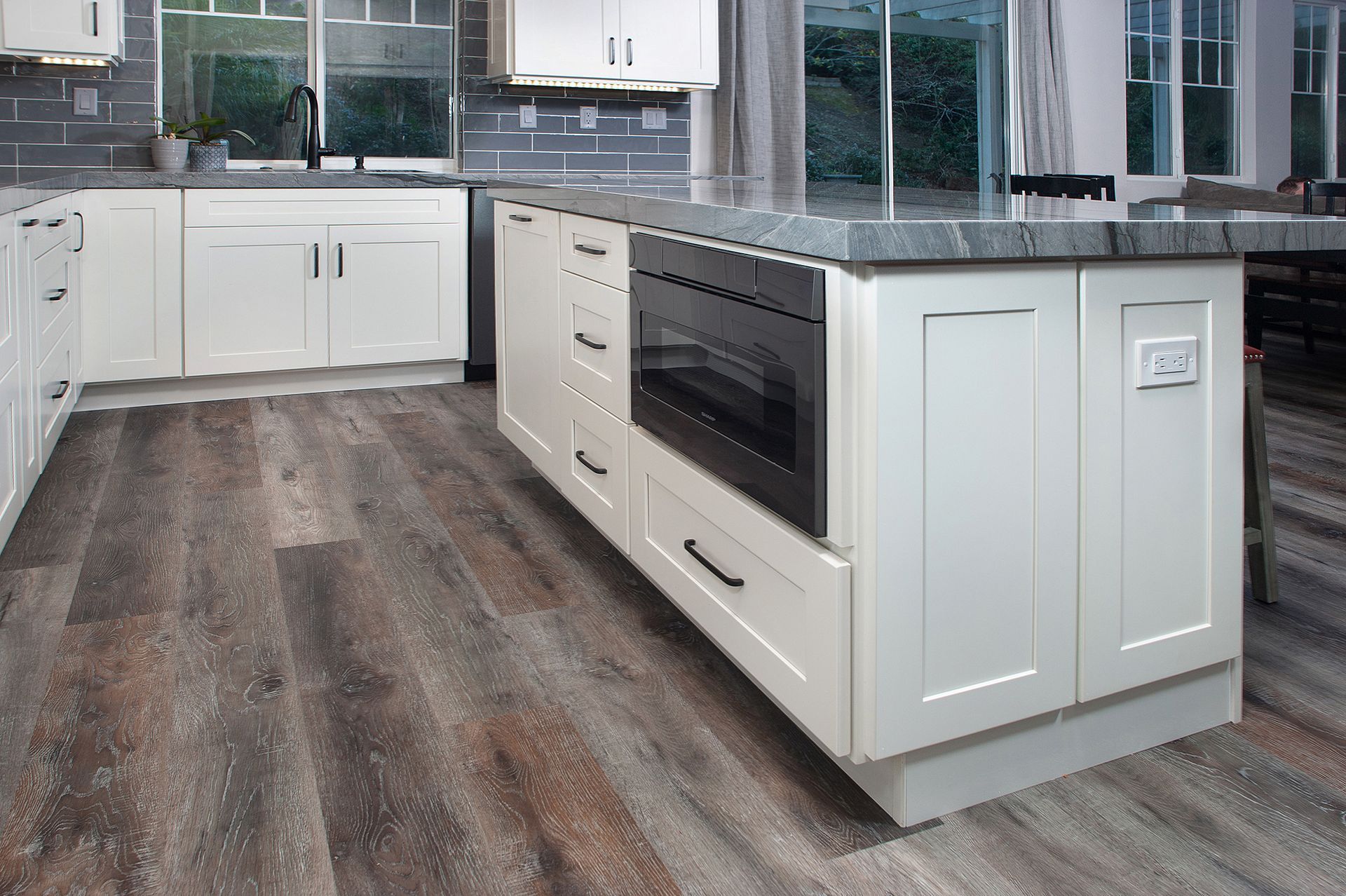 Modern kitchen with white cabinets, island with oven, wood-look flooring, and windows.