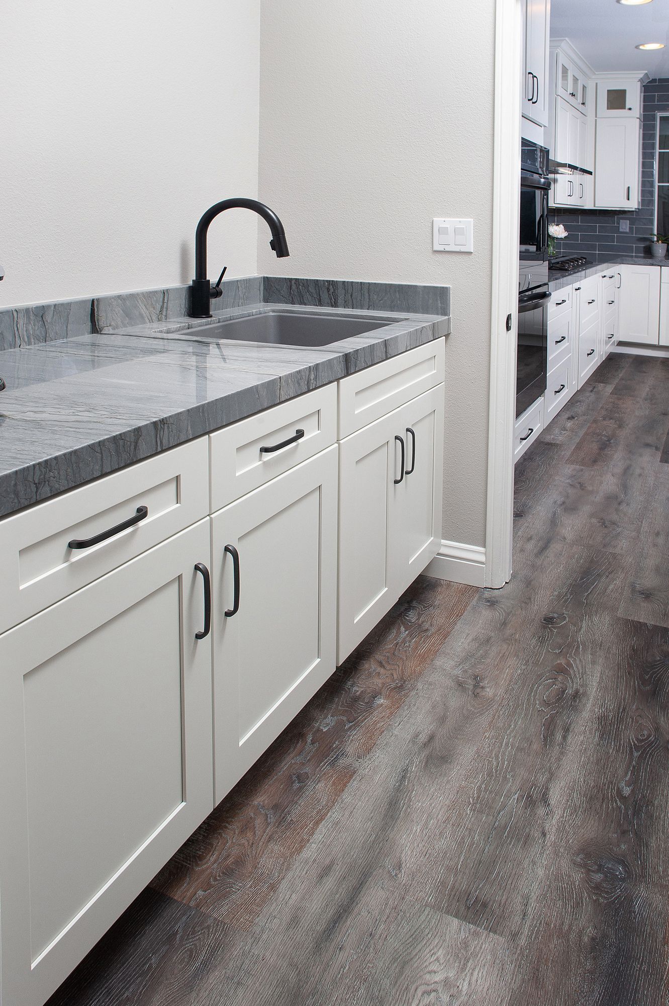 White kitchen cabinets with a dark countertop and black faucet, gray flooring.