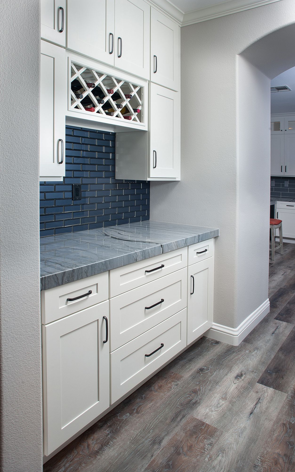 White built-in bar with gray countertop, wine rack, and blue mosaic backsplash in a home.