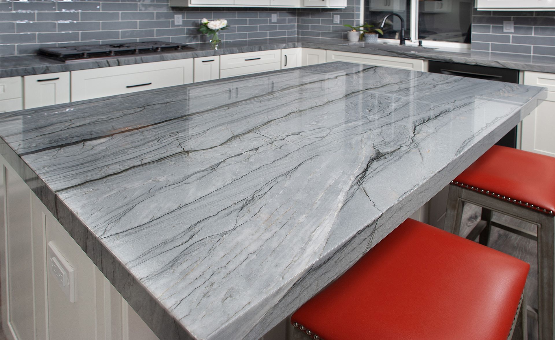 Kitchen island with a gray marble countertop, red stools, and white cabinets.