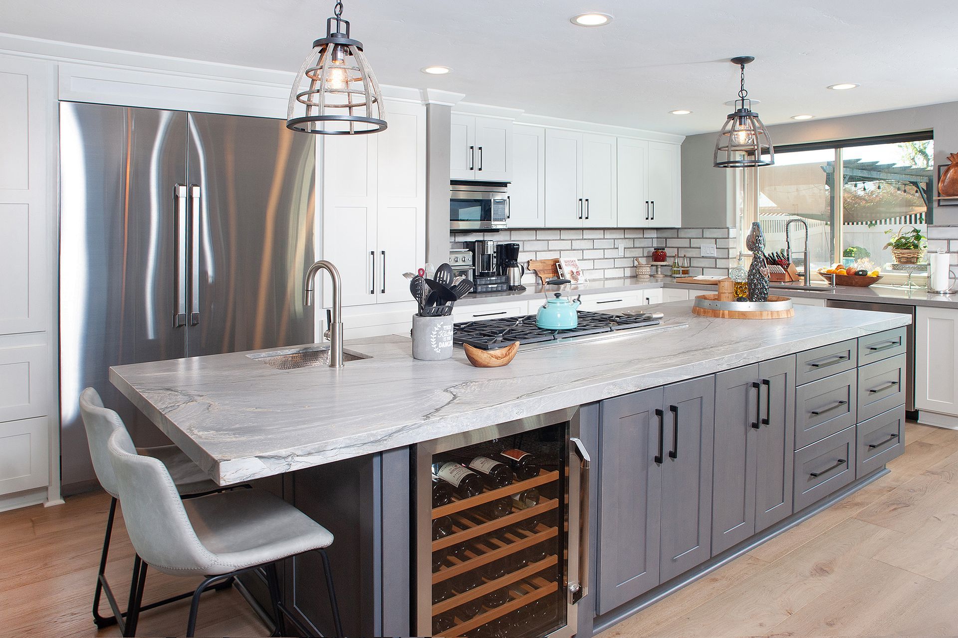 Modern kitchen with a large gray island, stainless steel refrigerator, and a wine cooler.