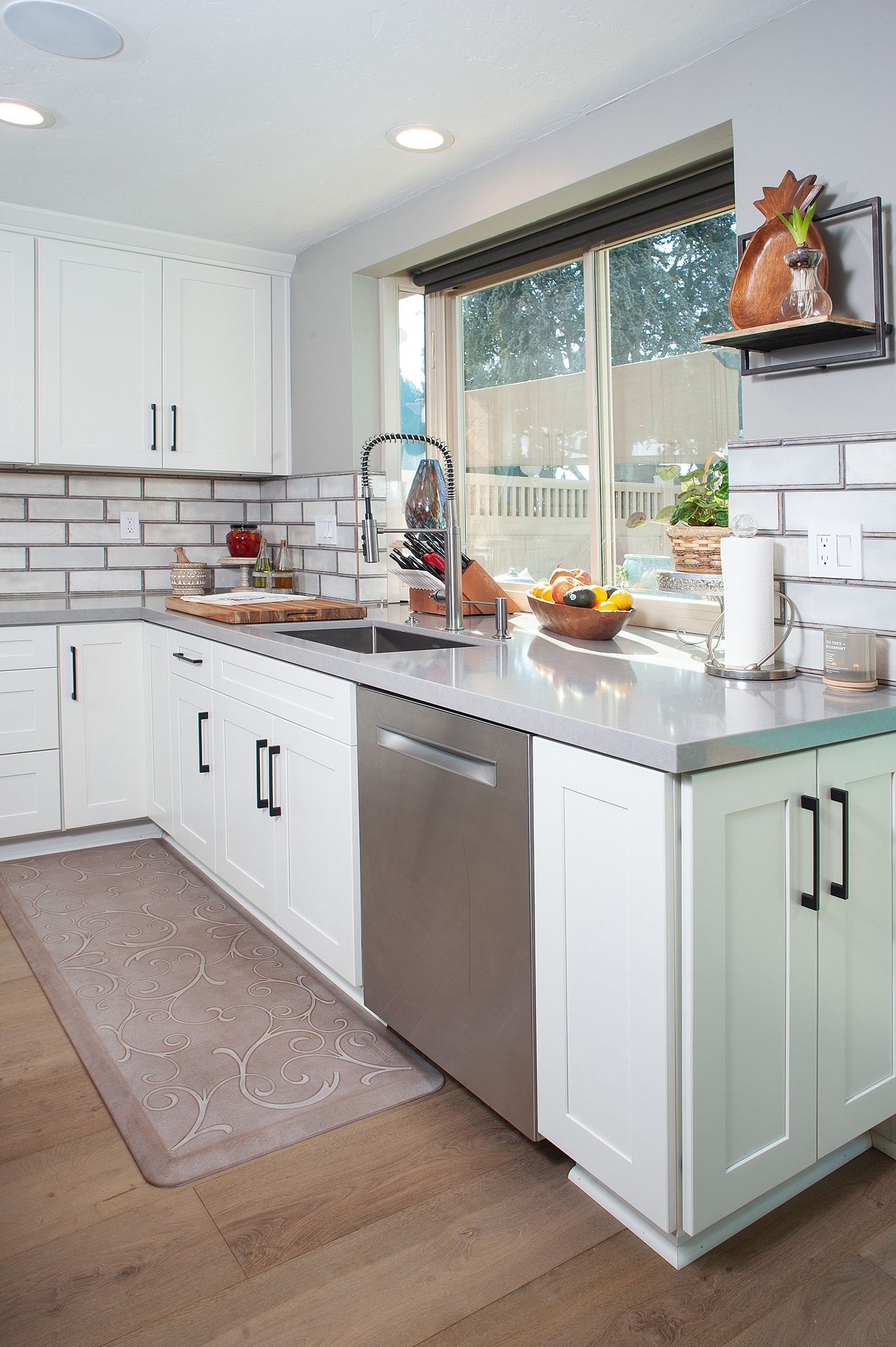 White kitchen with stainless steel appliances and a window overlooking a backyard.