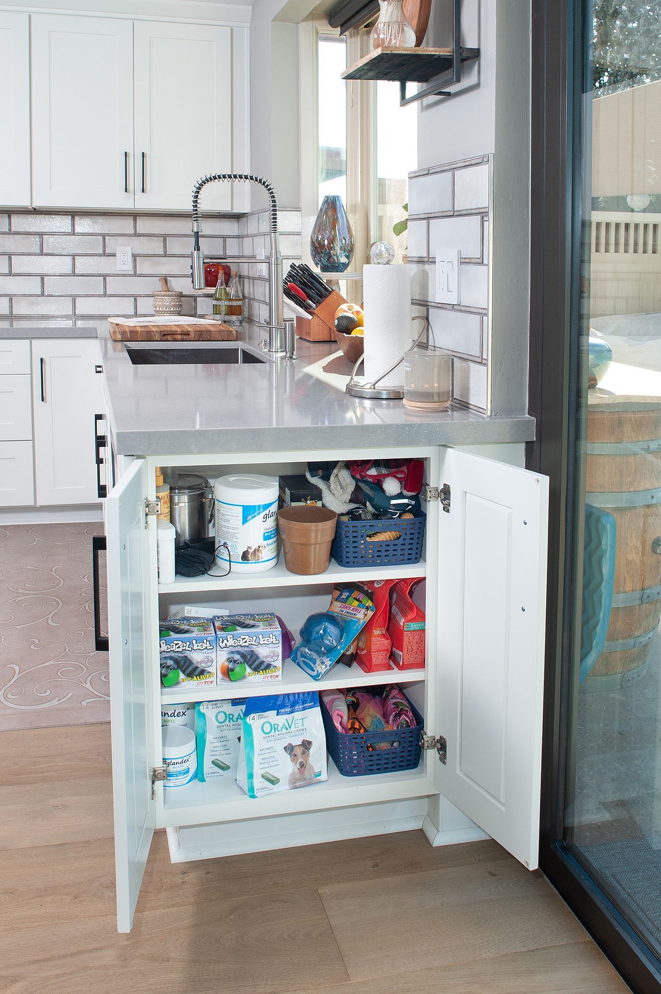 White kitchen cabinet open, filled with pet supplies, by a kitchen counter.