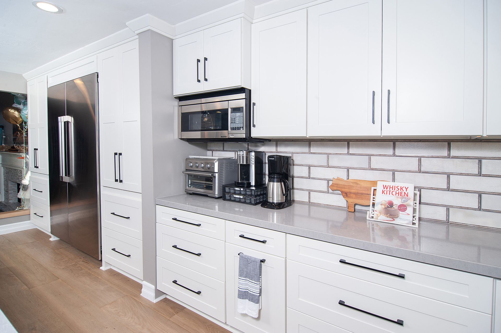 White kitchen with stainless steel fridge, microwave, and appliances on a gray countertop.