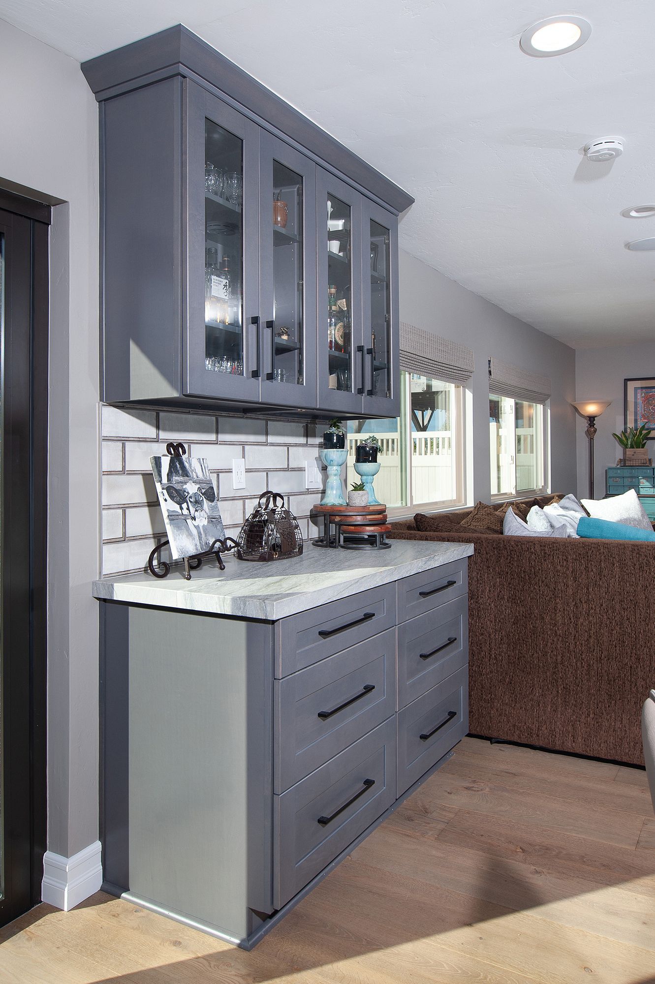 Gray cabinet with drawers, glass-front upper cabinets, and a white countertop in a kitchen.