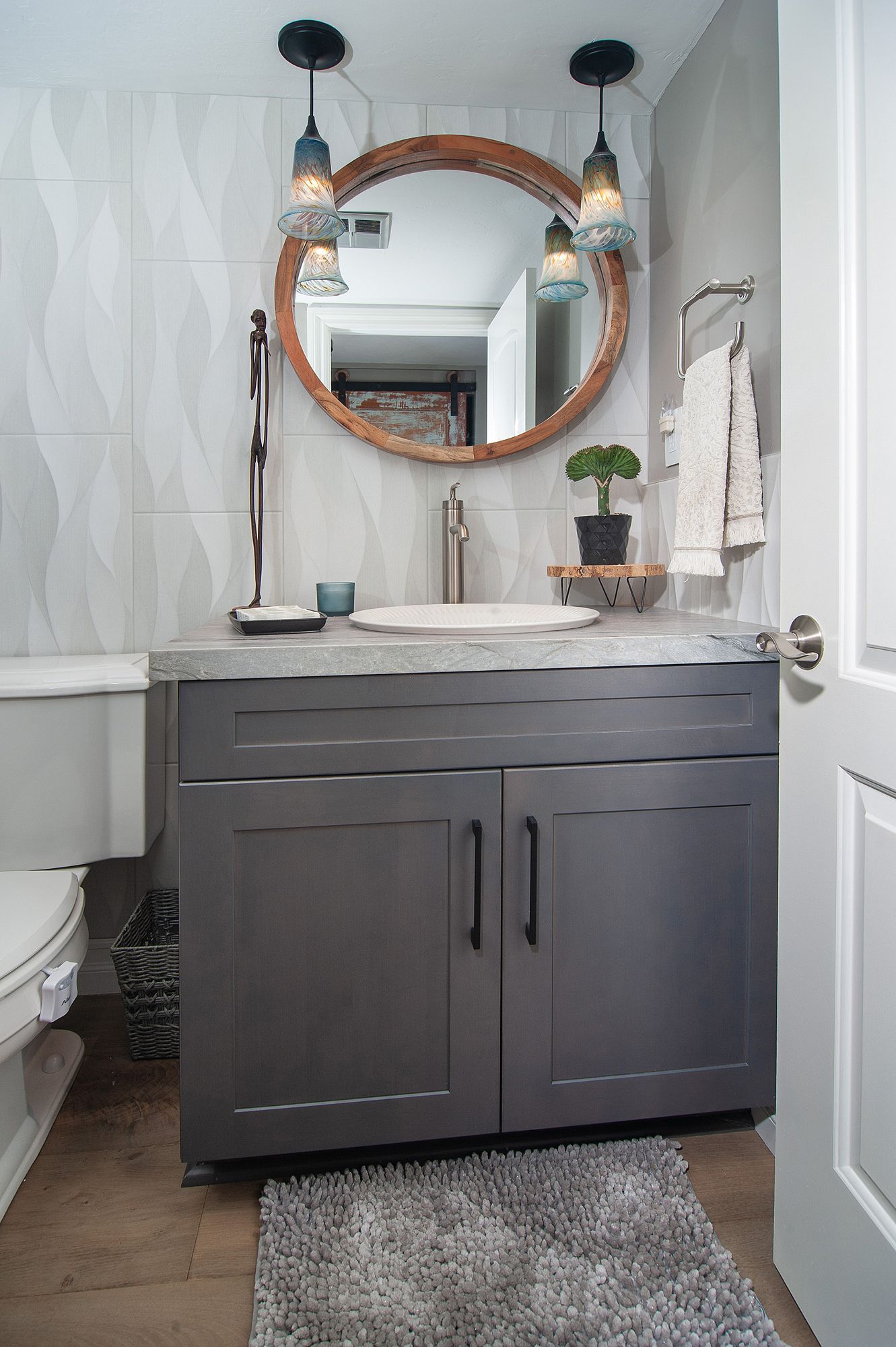 Gray bathroom with a gray vanity, round mirror, and patterned wall tile.