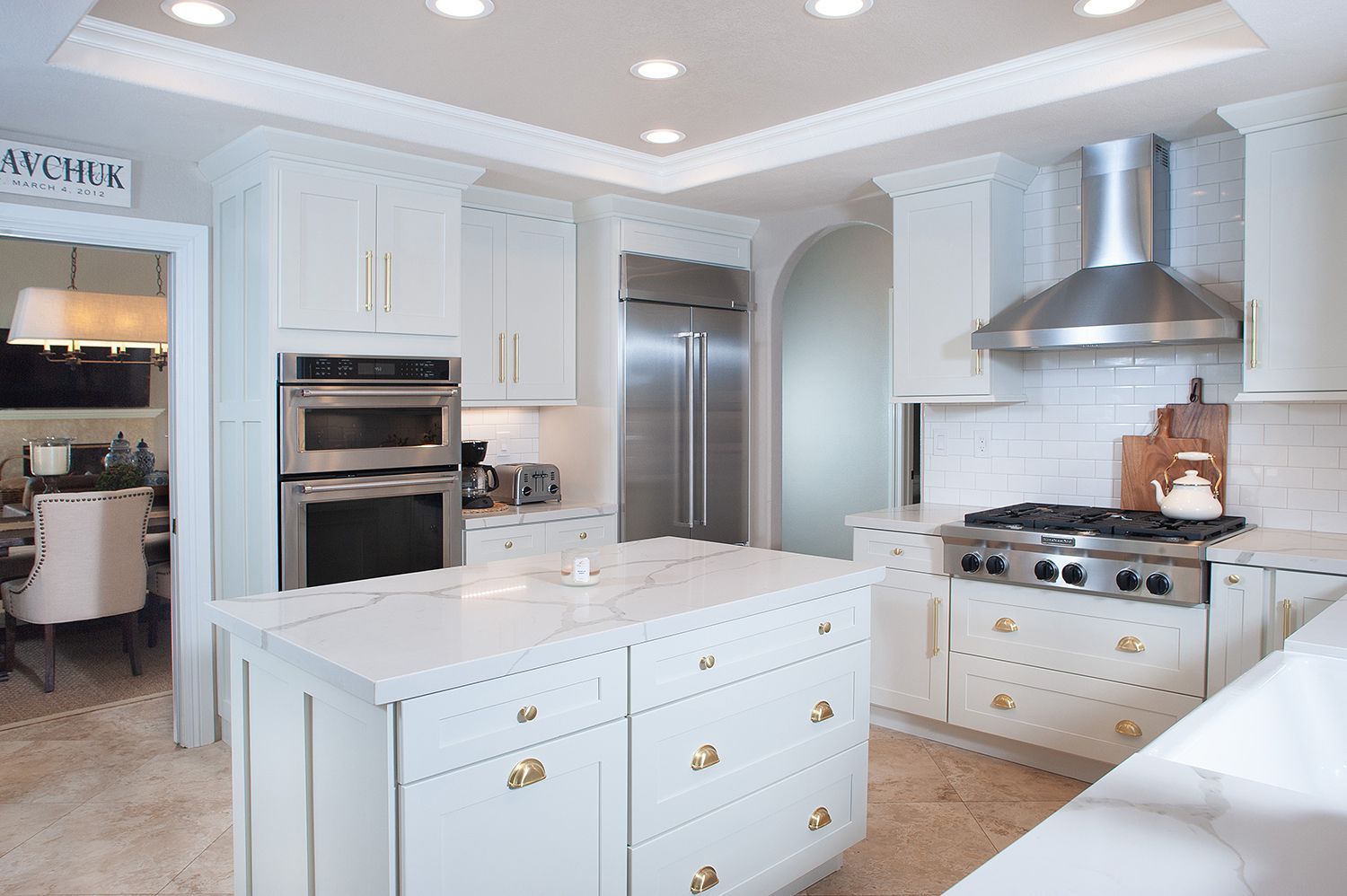 Bright white kitchen with stainless steel appliances, marble countertops, and a central island.