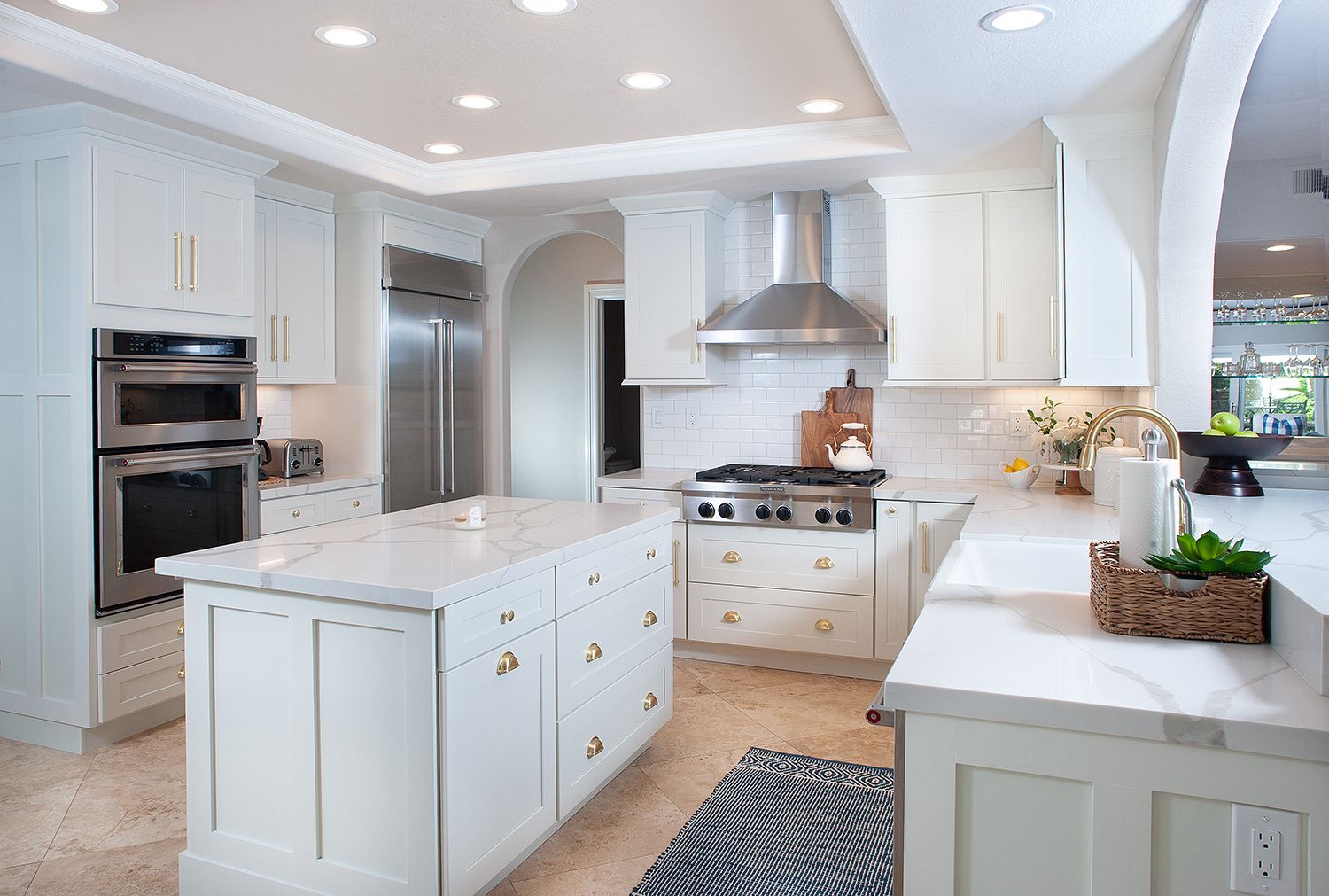 White kitchen with island, stainless appliances, and marble countertops.