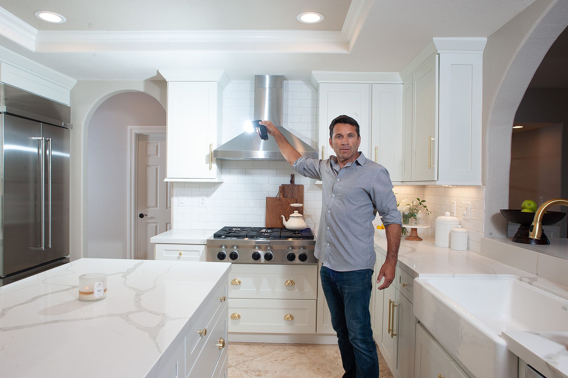 Man in kitchen inspecting vent hood; white cabinets, stainless steel appliances, light.