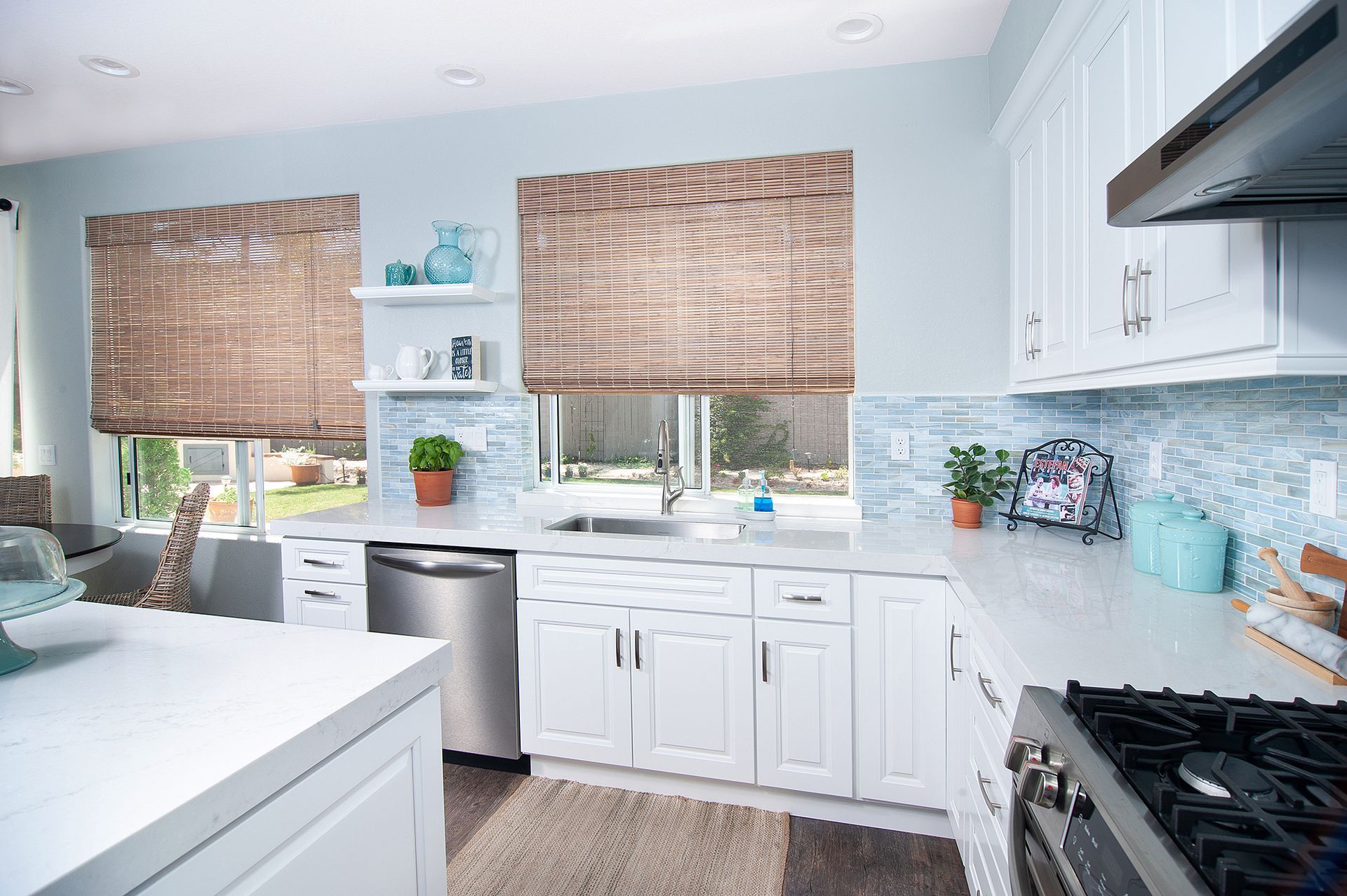 Light blue kitchen with white cabinets, woven shades, stainless steel appliances.