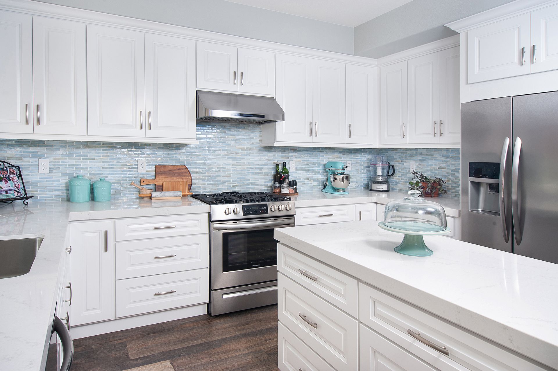 White kitchen with stainless steel appliances, blue backsplash, and island with countertop.