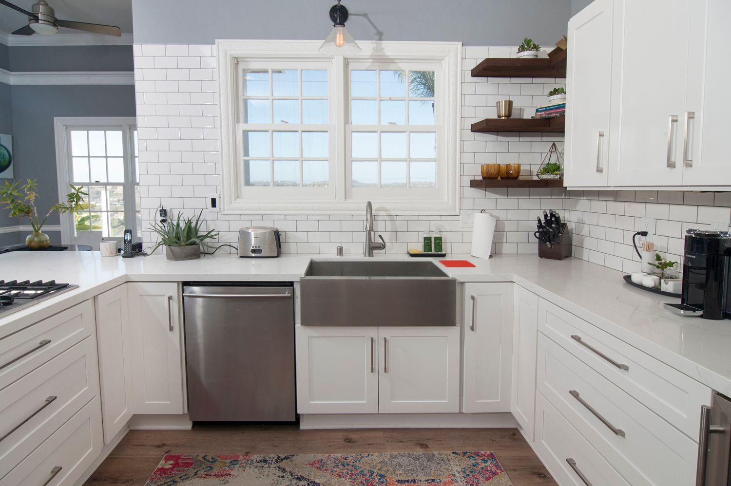 White kitchen with stainless steel sink, dishwasher, white cabinets, and window.