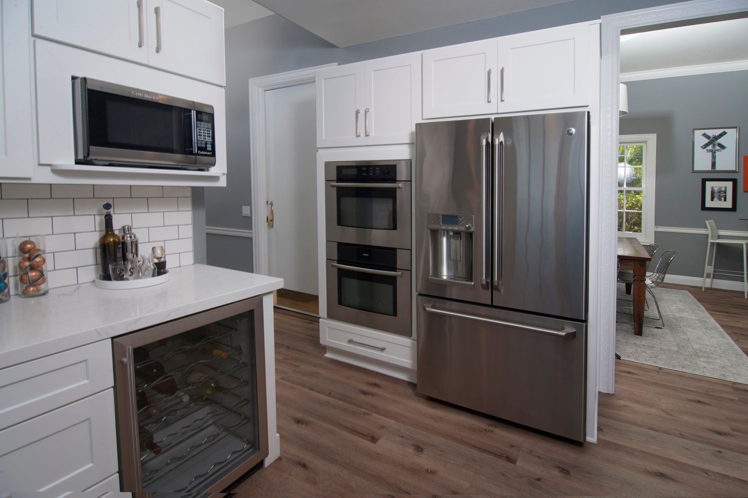 White kitchen with stainless steel appliances, including refrigerator and microwave, near an open doorway.
