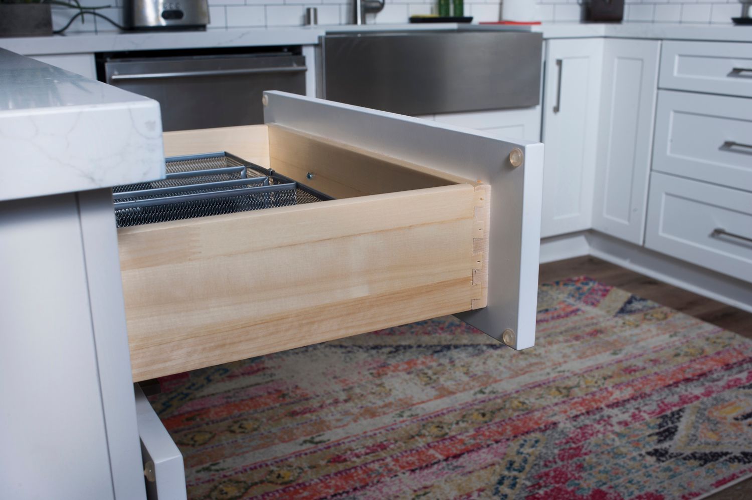Open kitchen drawer revealing a silverware organizer; white cabinetry, rug in foreground.