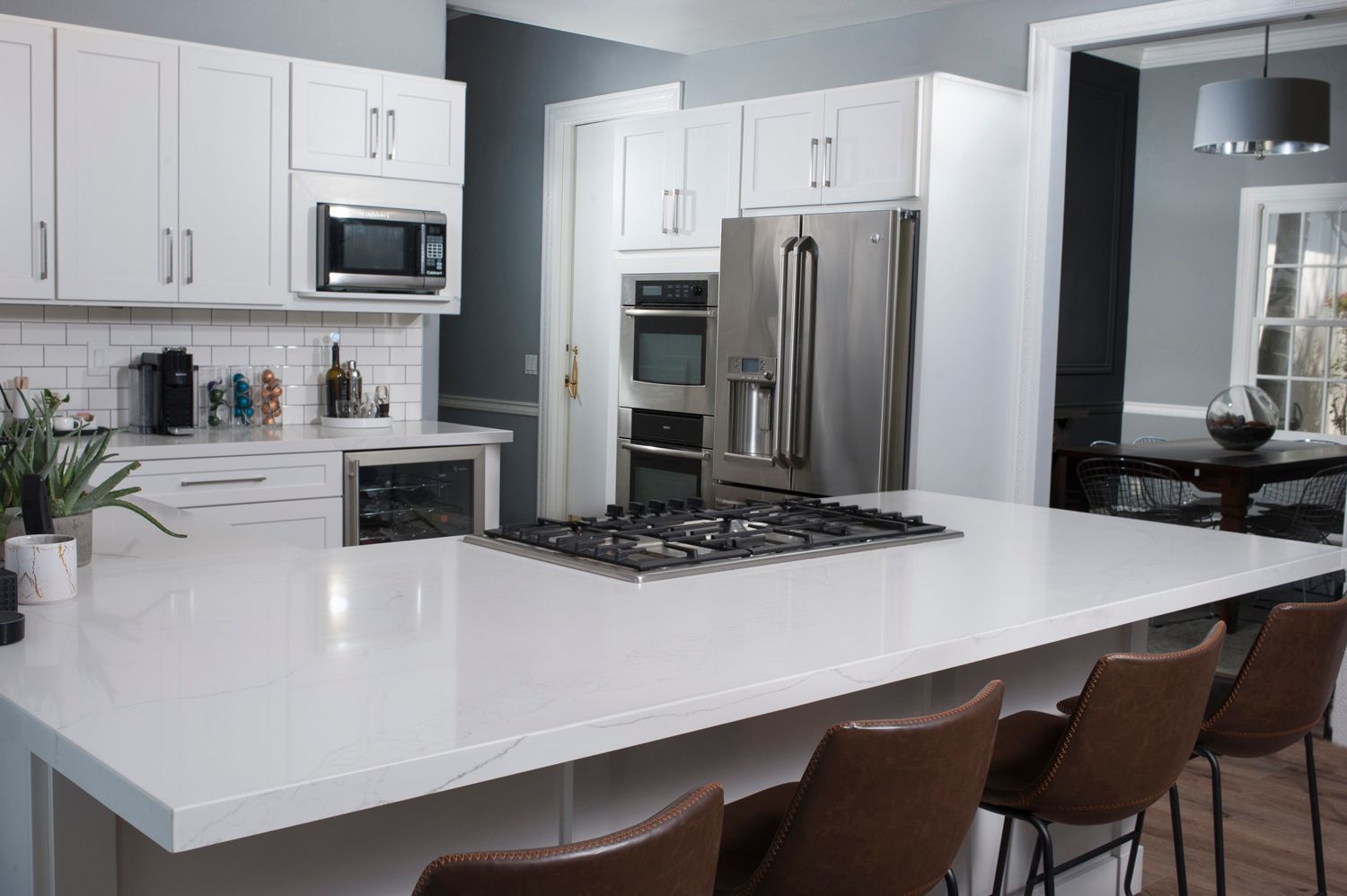 Modern kitchen with white cabinets, stainless steel appliances, island with stovetop, and brown bar stools.