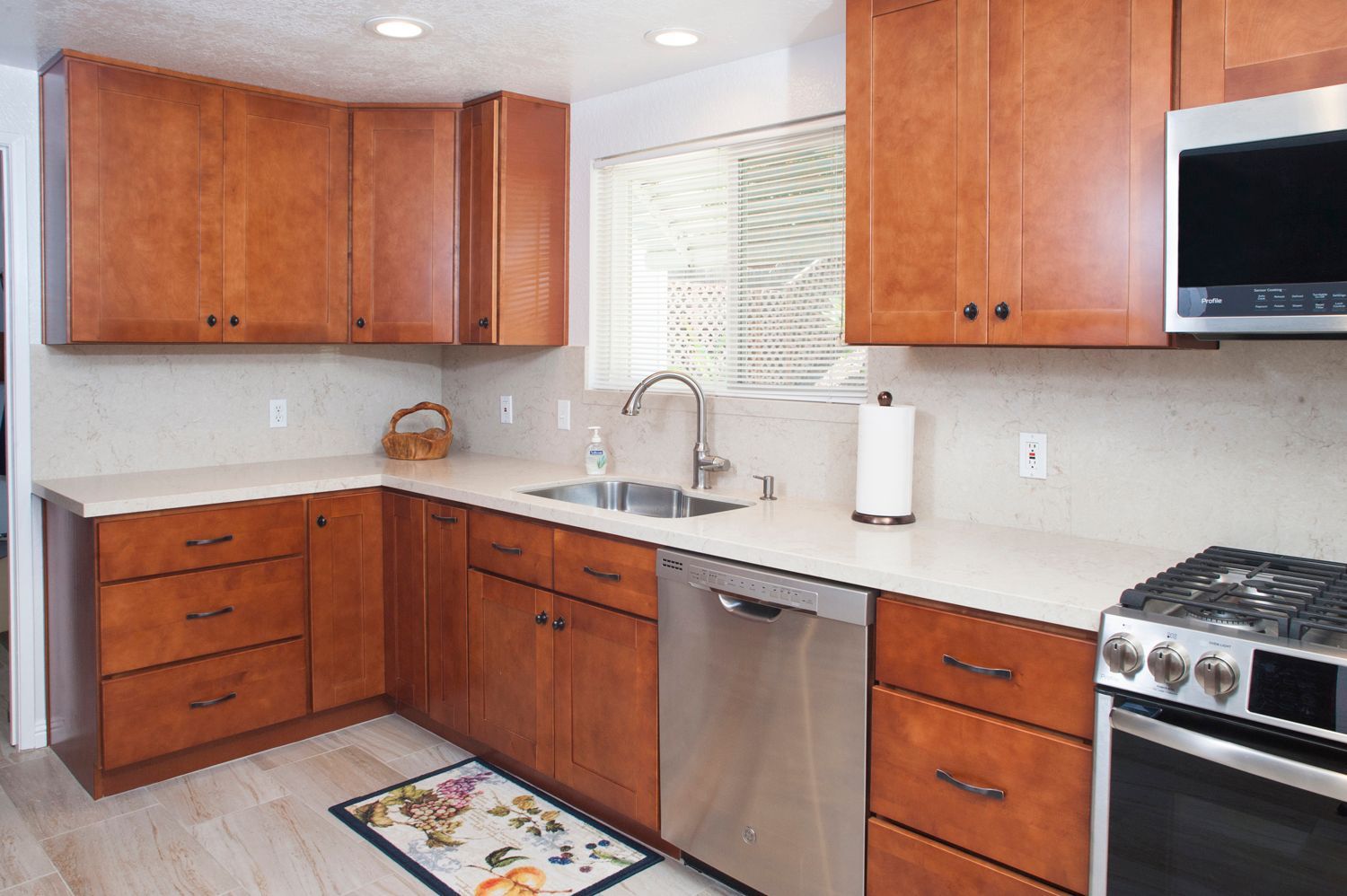 Kitchen with medium-tone wood cabinets, light countertops, stainless steel appliances, and a window above the sink.