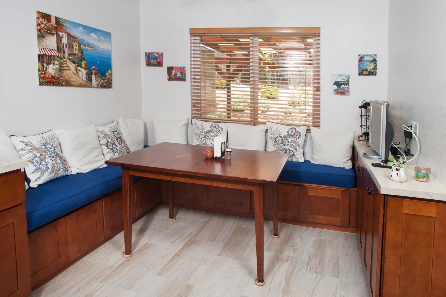 Cozy dining nook with a wooden table, built-in blue bench seating, and a window with blinds.