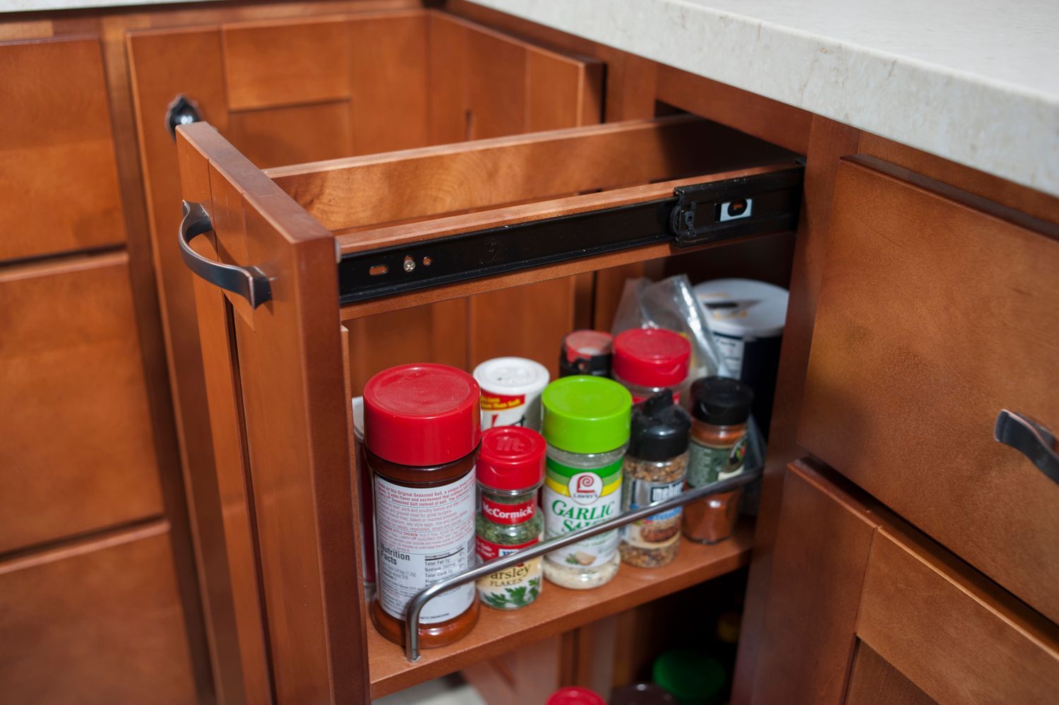 Spice rack pull-out cabinet in a kitchen, filled with various spice jars and containers.