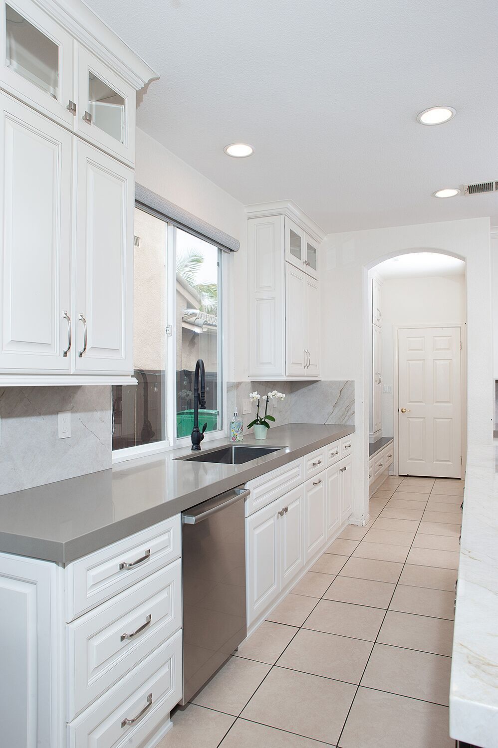 White kitchen with light gray countertops, stainless steel appliances, and a long, tiled floor.