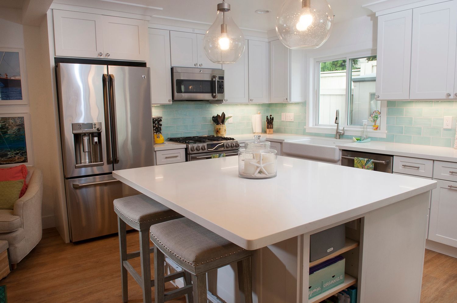 Modern white kitchen with island, stainless steel appliances, and light blue backsplash.