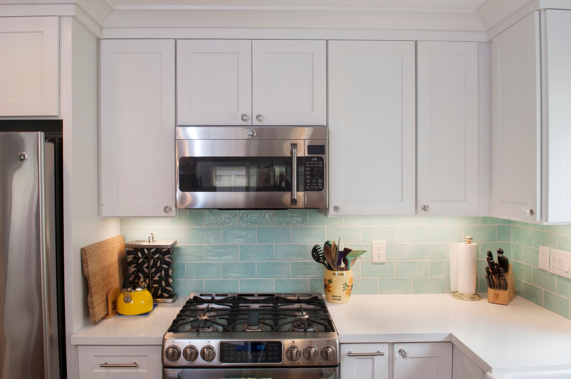 White kitchen with stainless steel appliances and turquoise backsplash.
