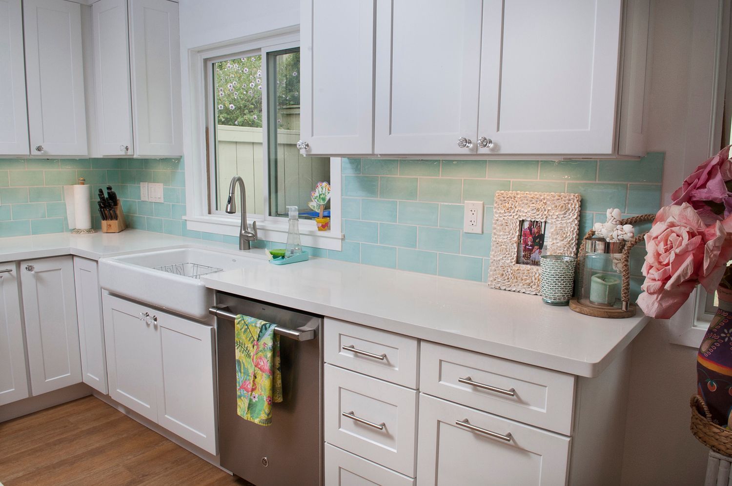 White kitchen with aqua tile backsplash, white countertops, stainless steel appliances, and a window.