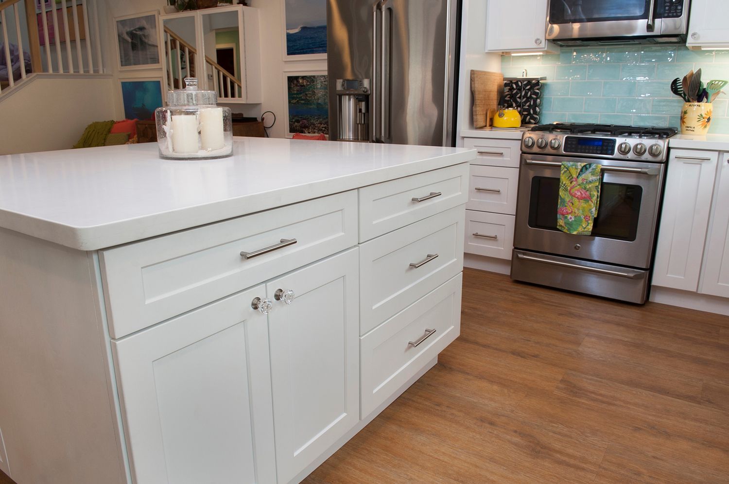 White kitchen island with drawers and cabinets, hardwood floors, stainless steel oven.
