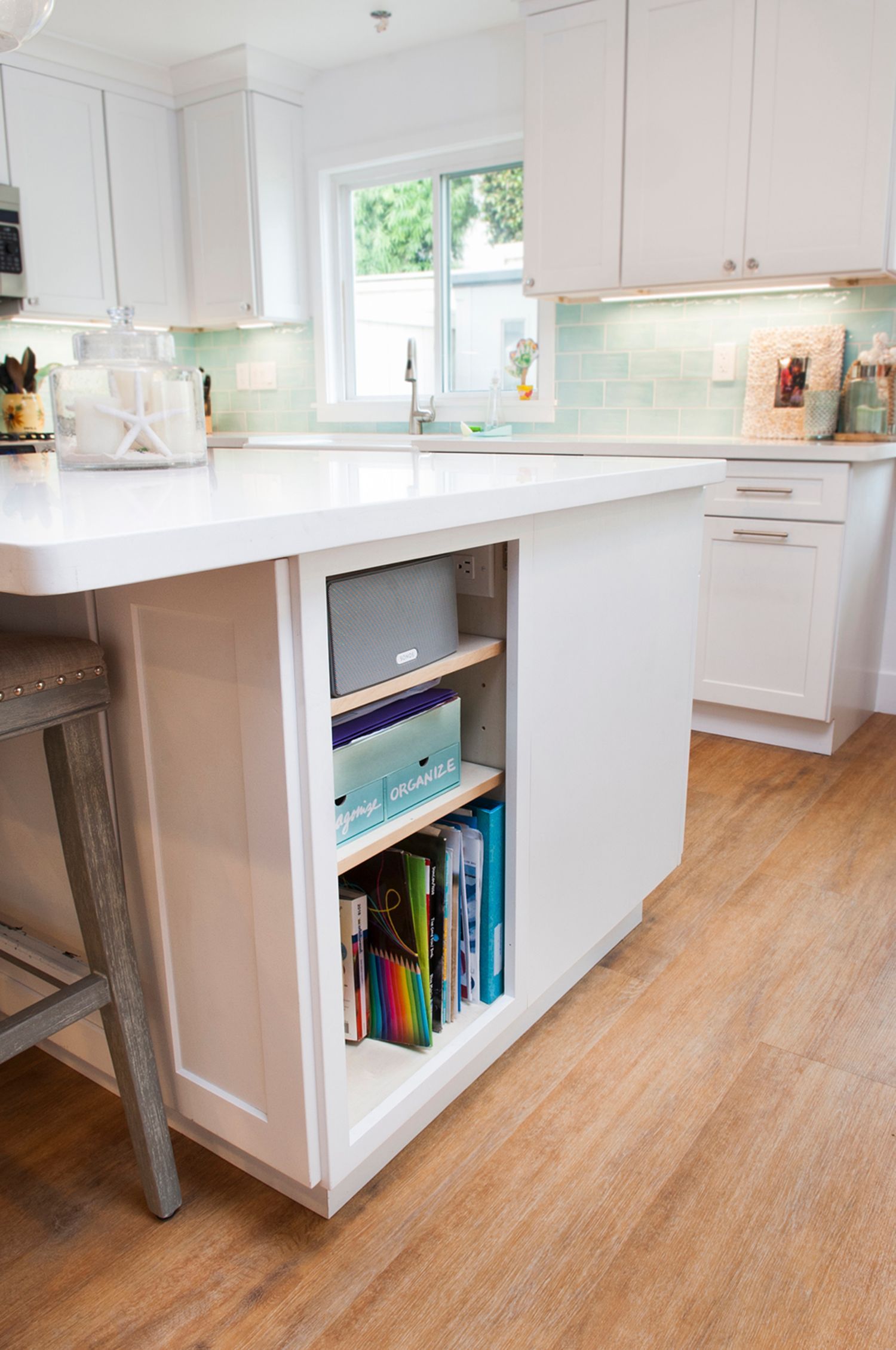 White kitchen island with open shelving holding books and boxes, with light wood floor.
