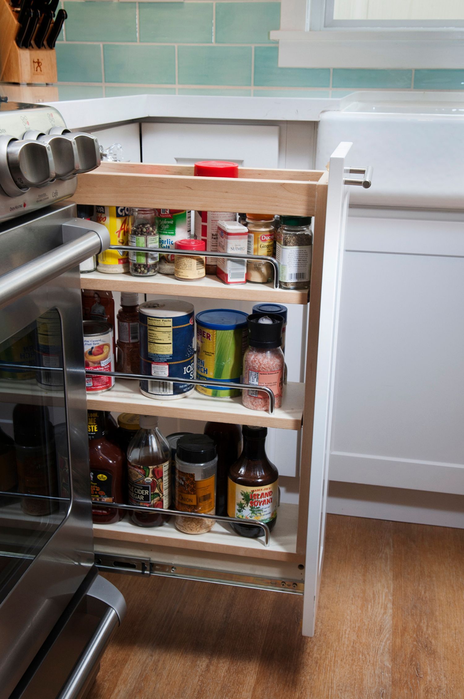 A pull-out spice rack in a kitchen, filled with various spice jars and bottles.