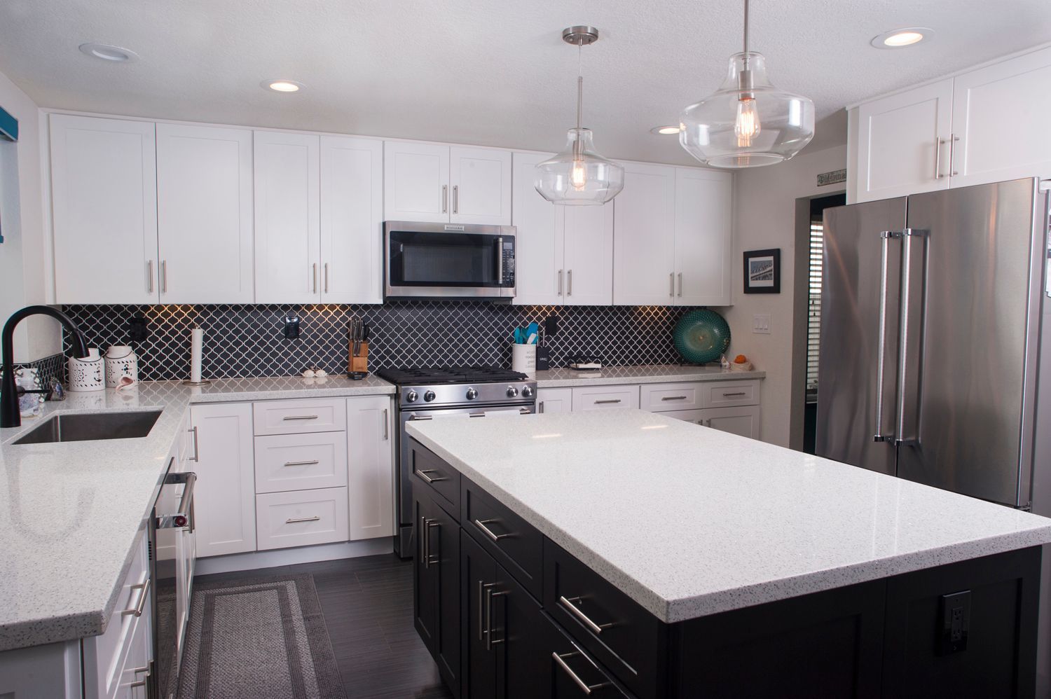 Modern kitchen with white cabinets, dark island, stainless steel appliances, and black and white backsplash.