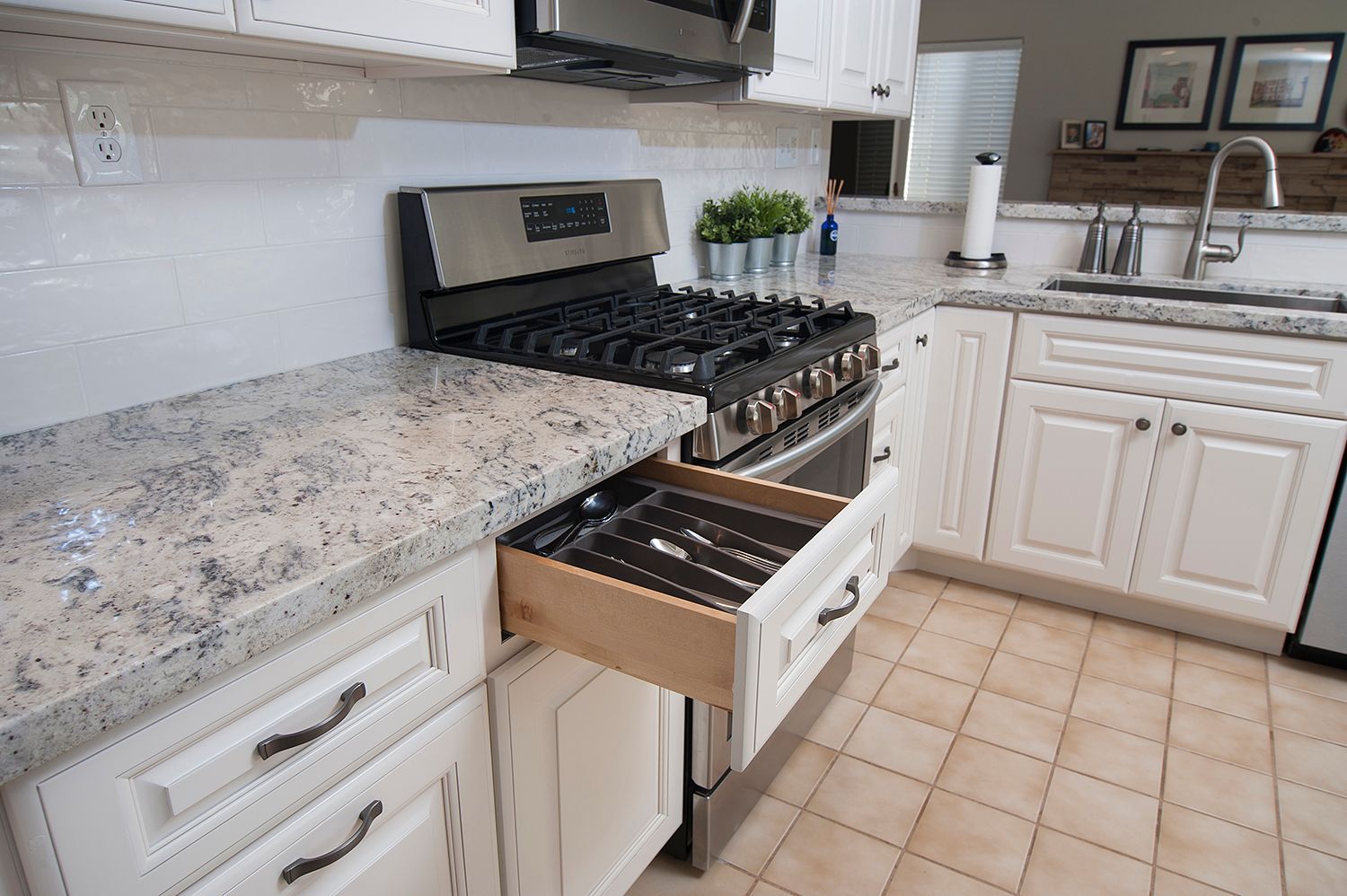 Kitchen with white cabinets, granite countertop, stove, and open drawer with silverware.
