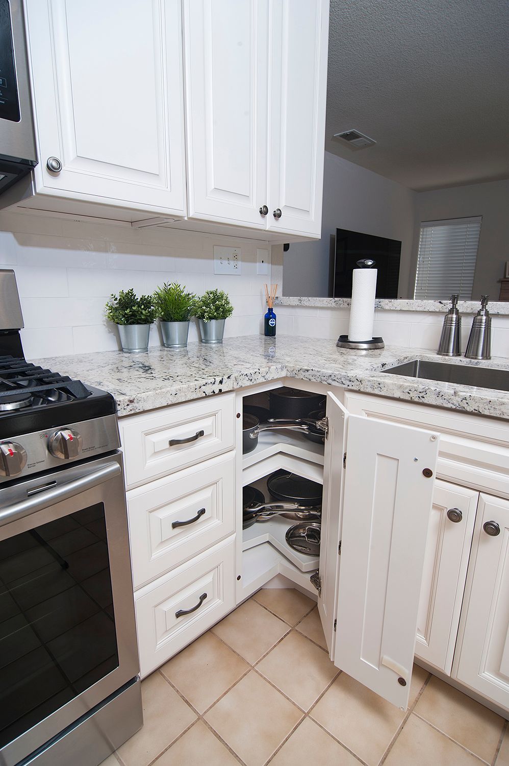 White kitchen cabinets, stainless steel appliances, granite countertop, corner cabinet open showing trays.