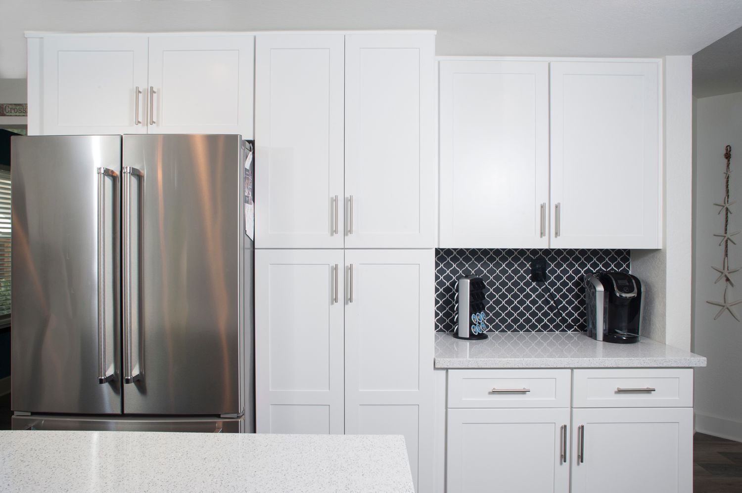 White kitchen with stainless steel refrigerator, cabinets, and countertop. Black tile backsplash.
