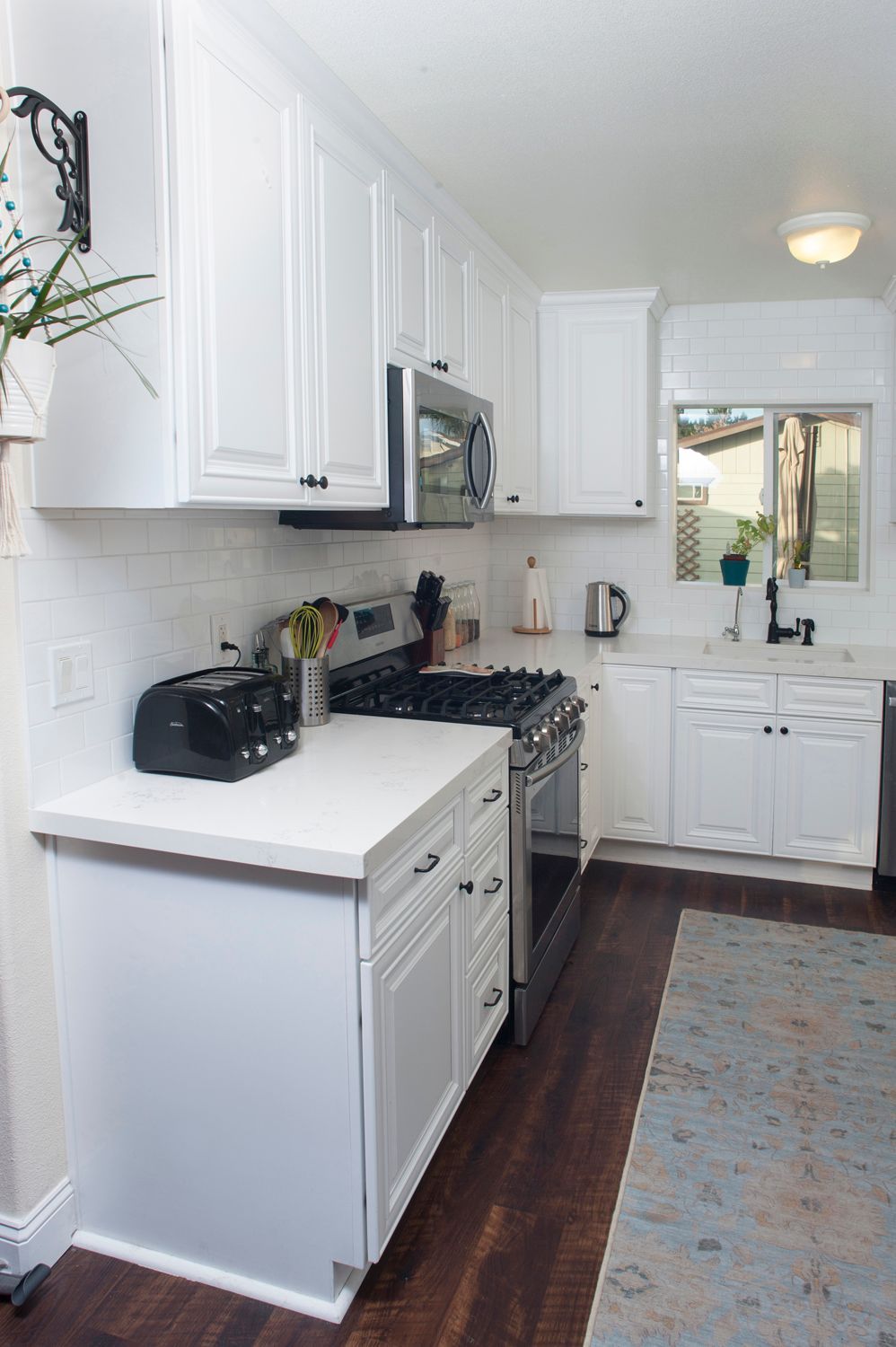 White kitchen with white cabinets, stainless steel appliances, and dark wood floors.